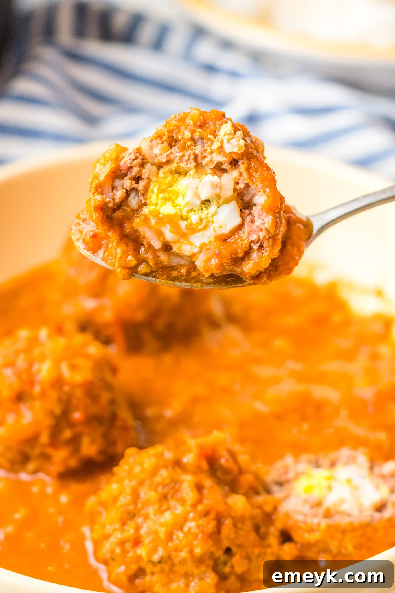 A delicious Albondigas en Chipotle meatball held on a spoon, showcasing its rich sauce.