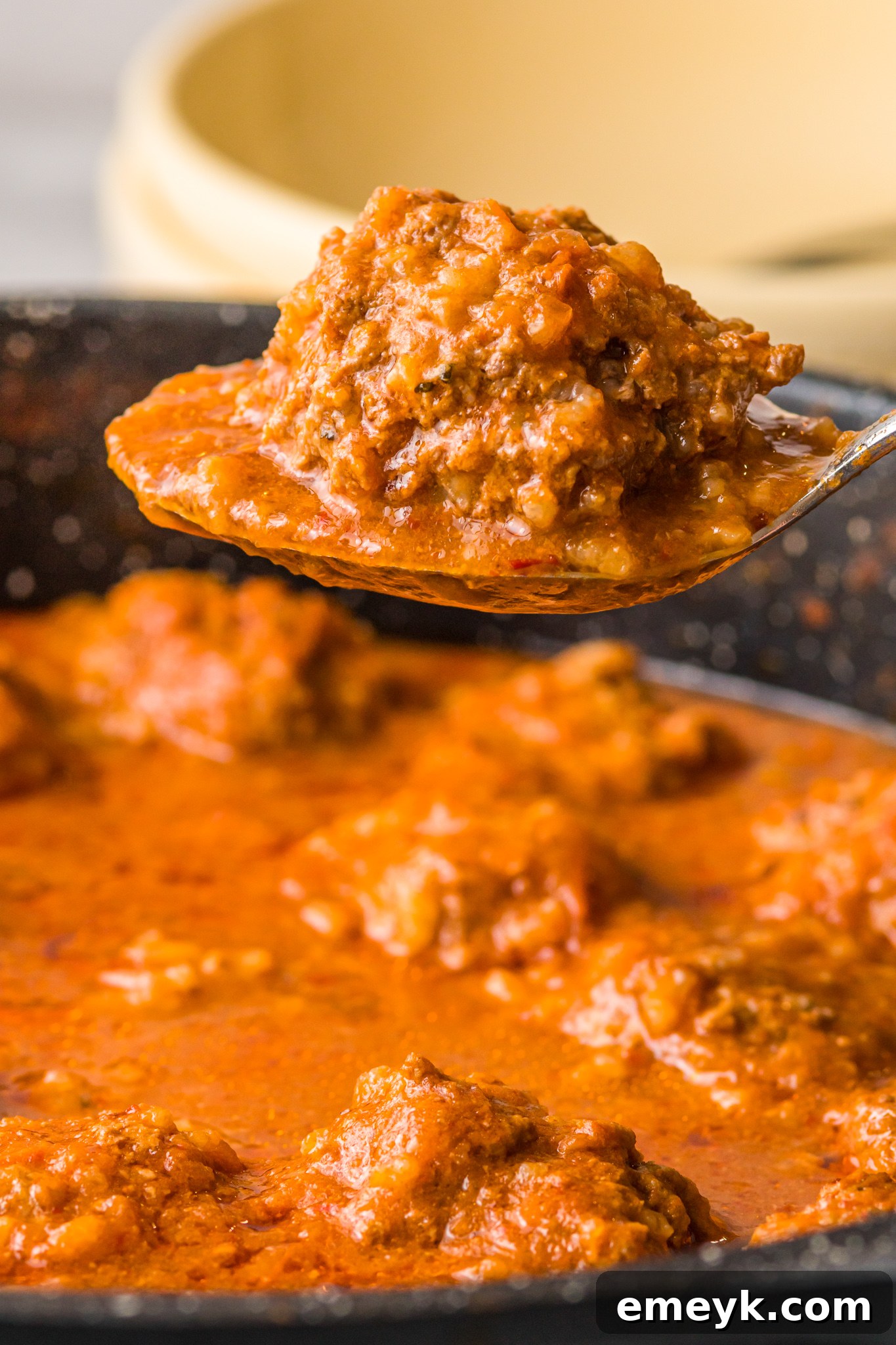 A serving spoon with an Albondigas en Chipotle meatball, hovering over the pan of simmering sauce.