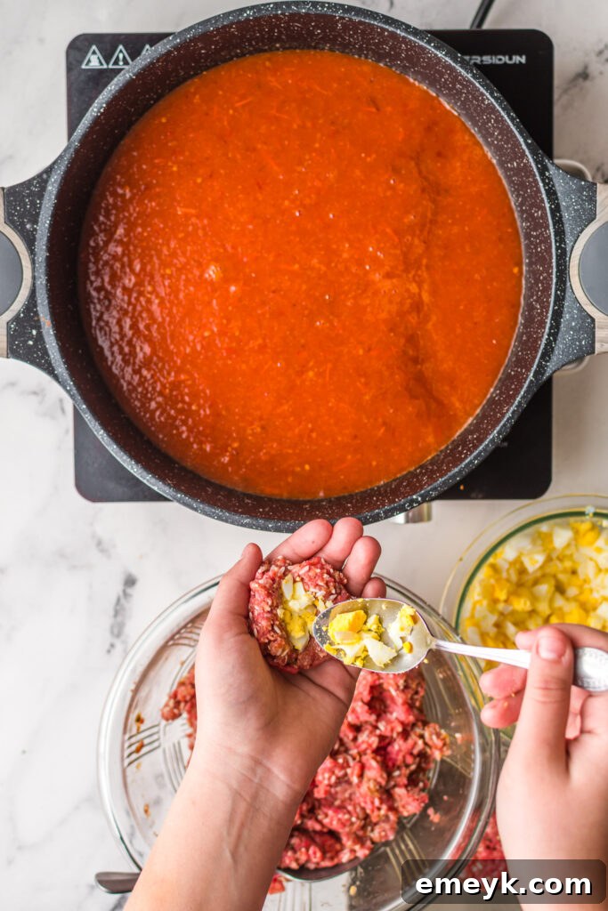 Chopped boiled egg being placed into the ground beef mixture to form a meatball.