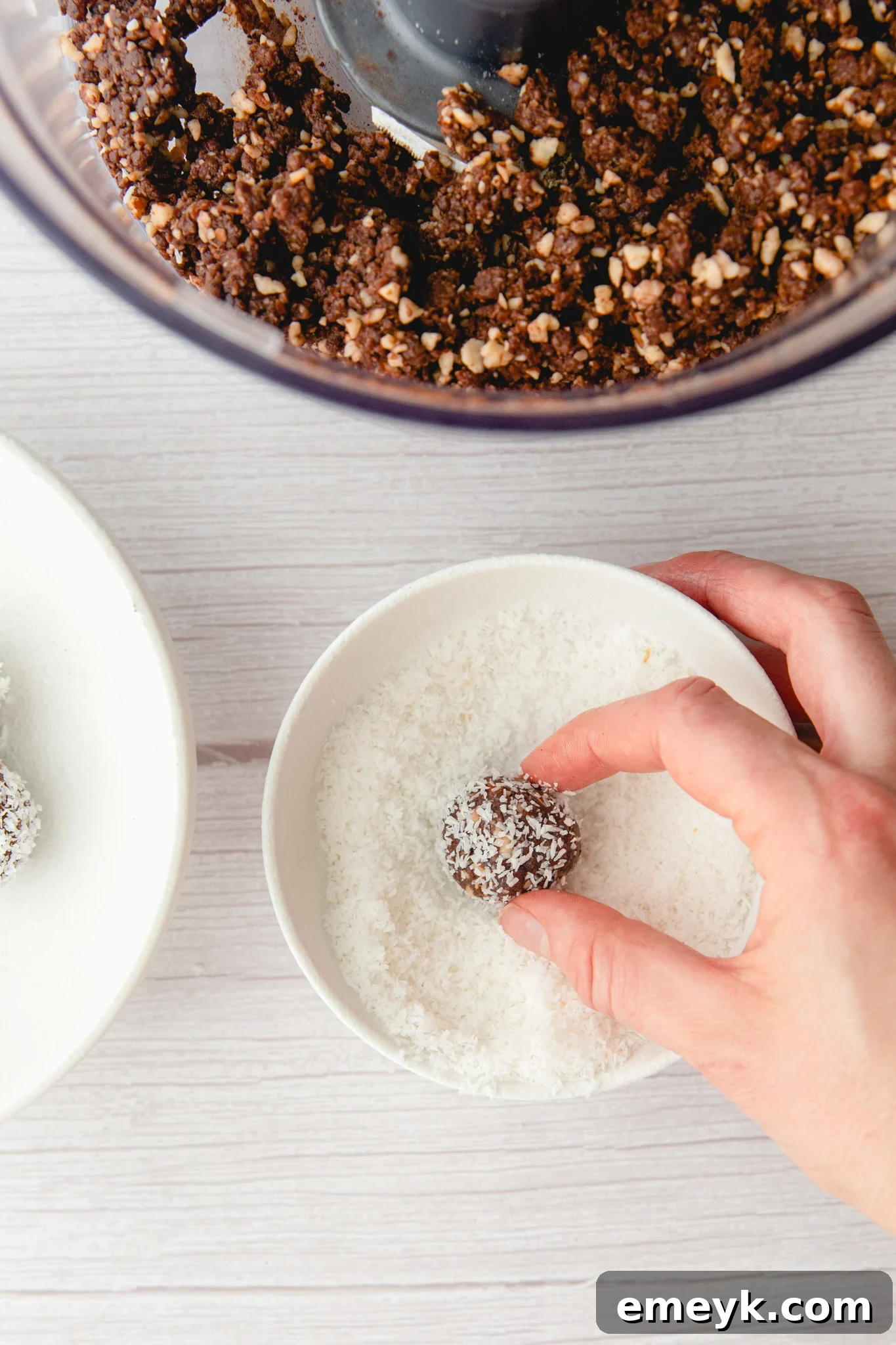 Freshly rolled Easy Date Protein Balls being dipped and coated in desiccated coconut.