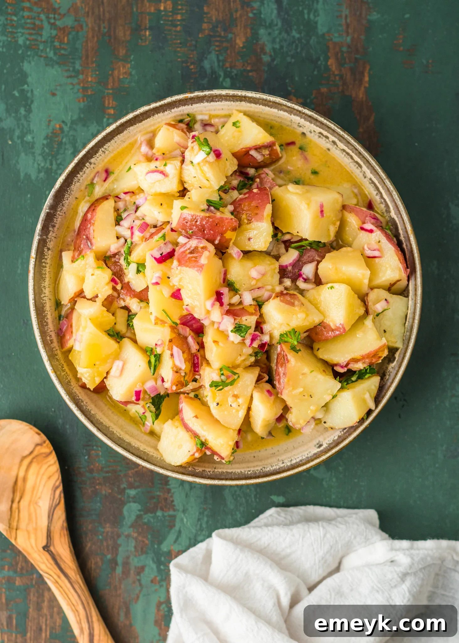 Authentic German Potato Salad 7 A serving of German Potato Salad being scooped with a wooden spoon, showcasing its hearty texture and vibrant ingredients.
