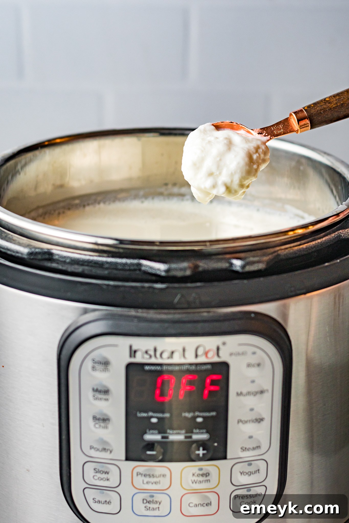 Yogurt starter being stirred into cooled milk in the Instant Pot inner pot, a crucial step for culturing.