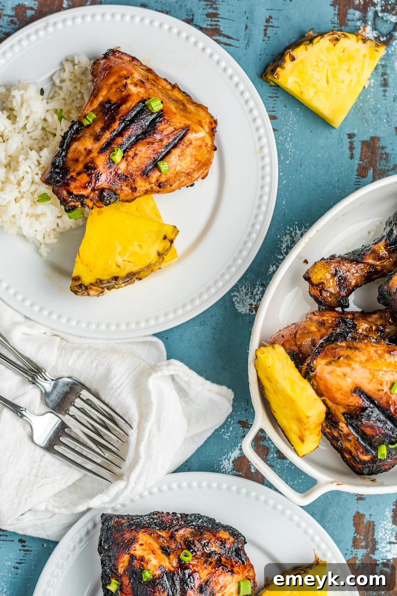 Golden Glazed Huli Huli Chicken 7 Individual servings of Grilled Huli Huli Chicken on white plates, accompanied by coconut rice and fresh pineapple chunks.