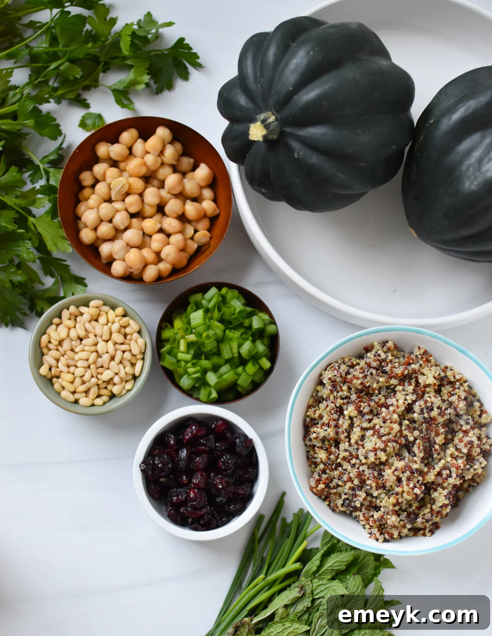 Raw ingredients laid out for Mediterranean Stuffed Acorn Squash, including squash, quinoa, chickpeas, herbs, and spices.