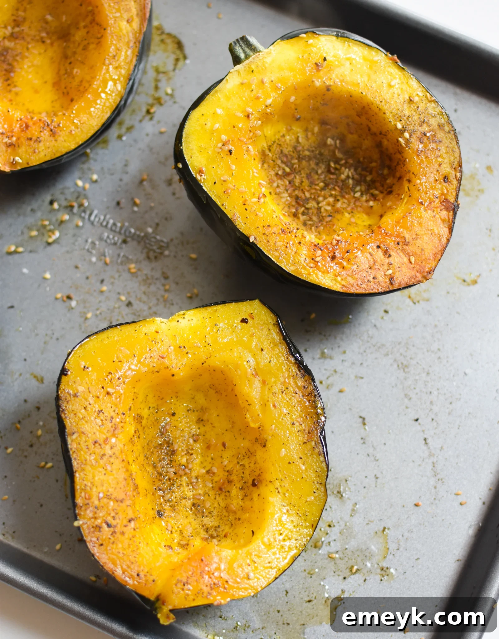 Acorn squash halves seasoned with salt and za'atar on a baking sheet before roasting.
