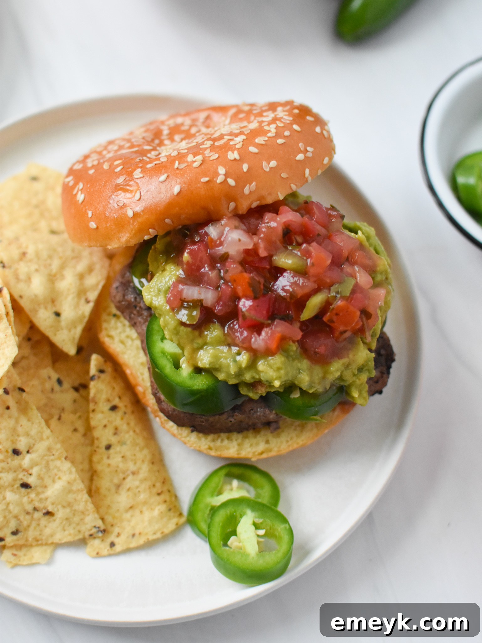 Close-up view of a Tex Mex Burger showcasing sliced jalapeños and lush green guacamole.