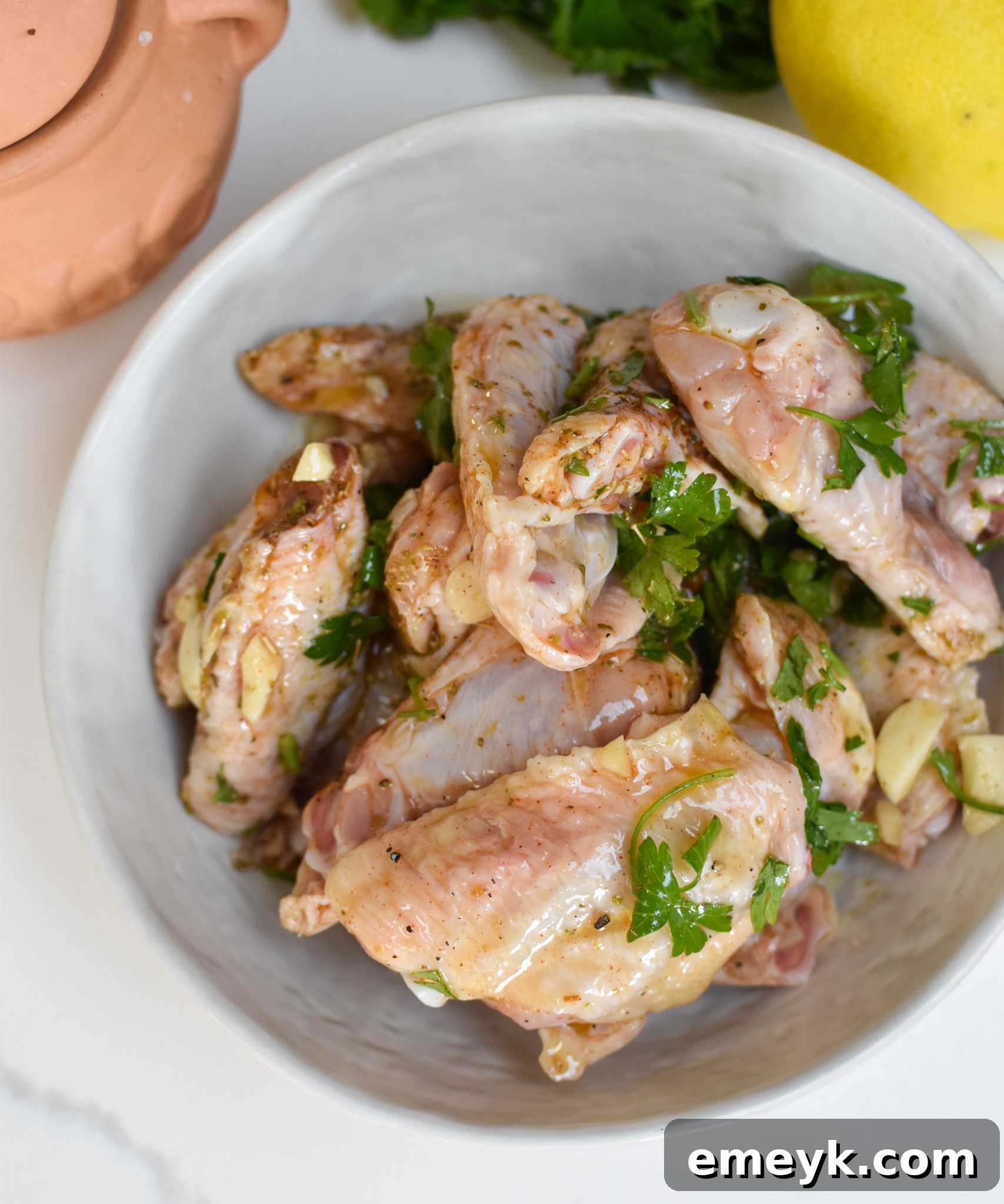 Chicken wings marinating in a bowl with Mediterranean spices and olive oil.