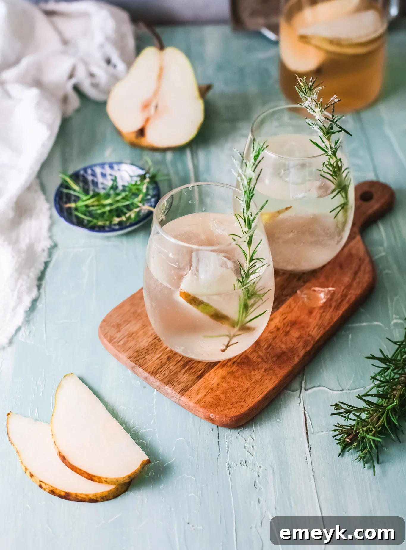 A glass of White Sangria Recipe garnished with pear slices and rosemary.