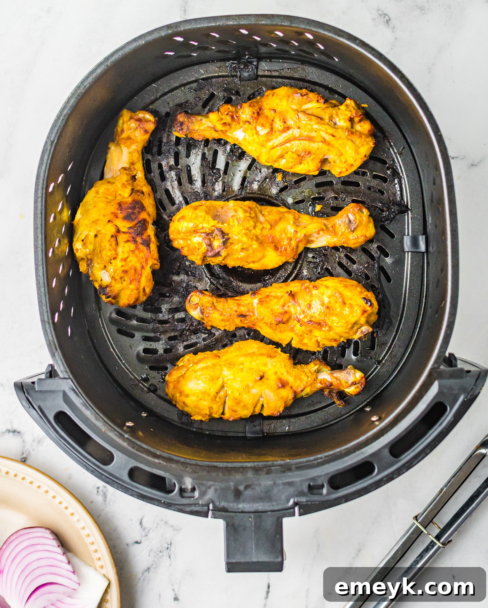 Crispy Air Fryer Tandoori Chicken Legs 9 Crispy Tandoori chicken legs cooking inside an air fryer basket, showing their golden-brown exterior.