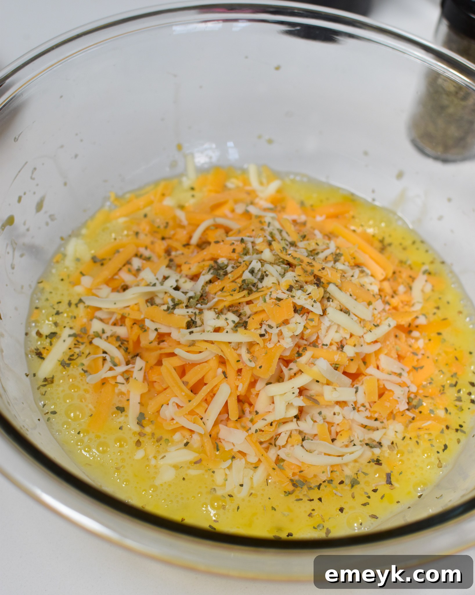 Egg and cheese mixture in a bowl, combined with herbs and spices for chaffles.