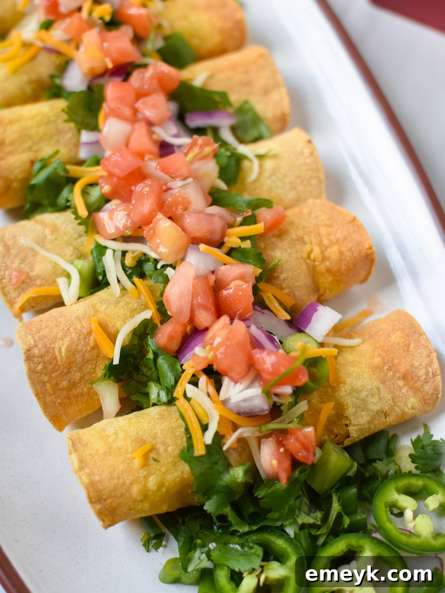 Crispy Air Fryer Pork Taquitos garnished with fresh pico de gallo and cilantro, served on a white platter.