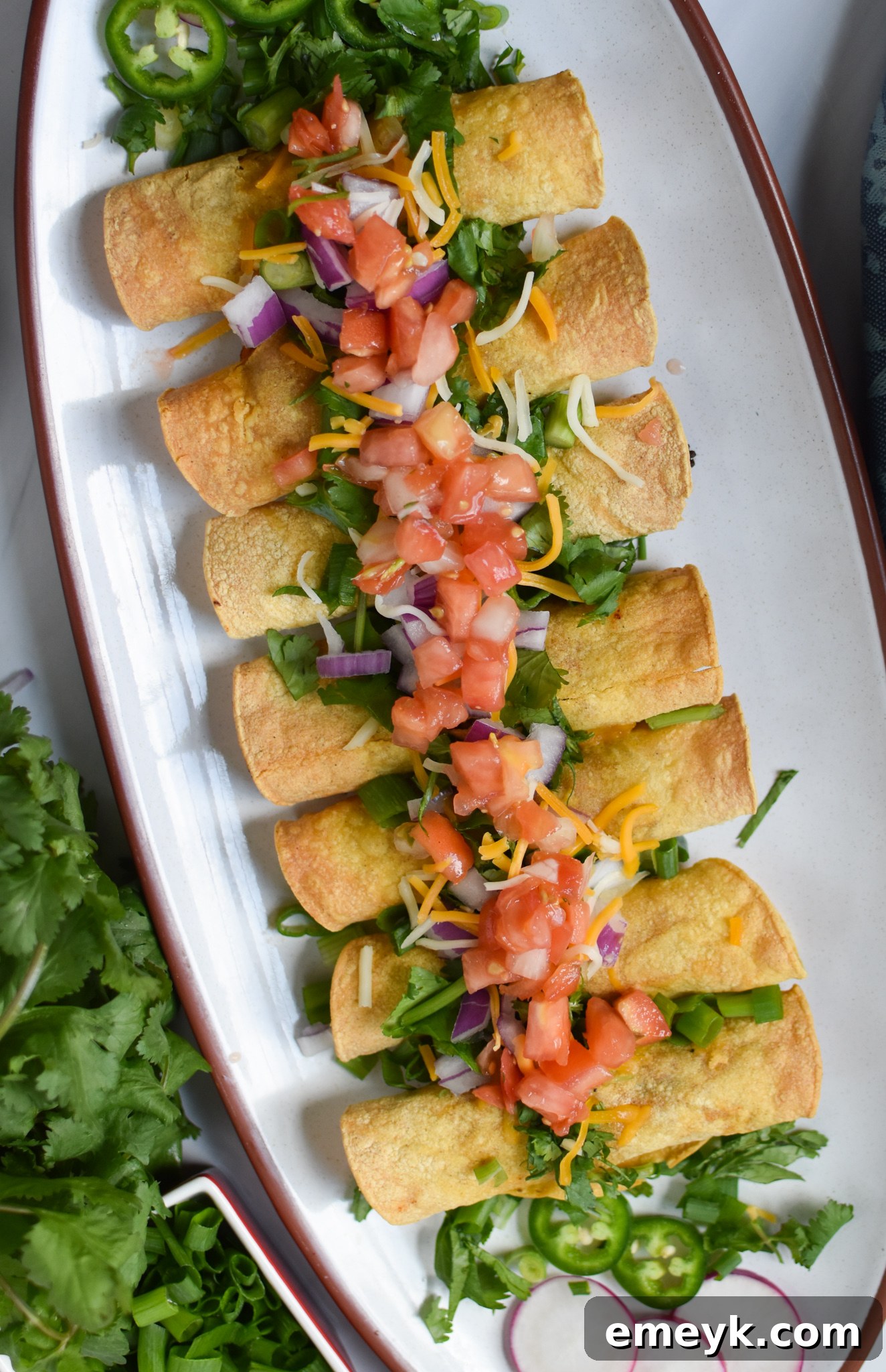 A beautiful platter of golden brown Air Fryer Pork Taquitos, garnished and ready for serving.