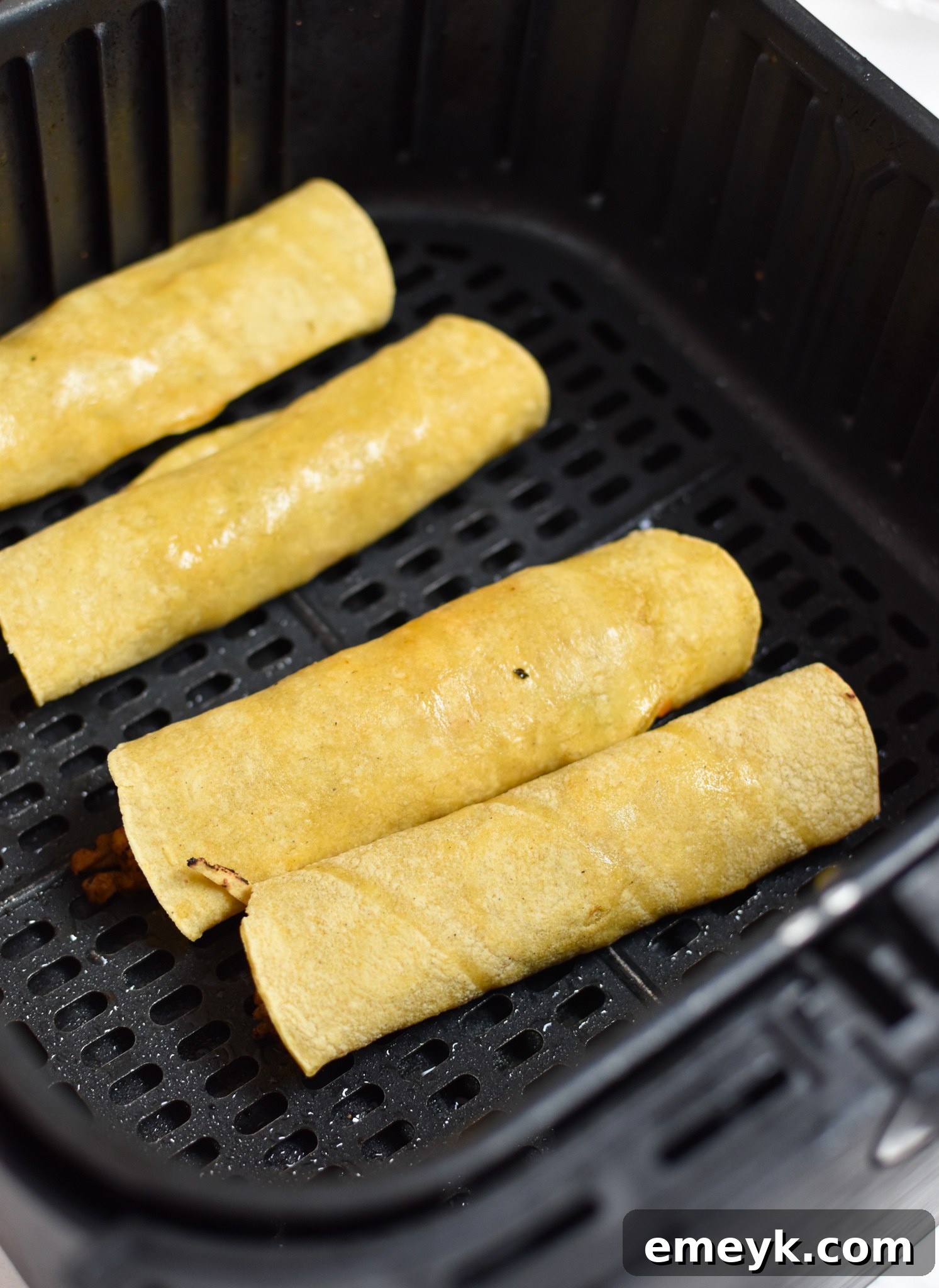 Rolled Air Fryer Pork Taquitos arranged in a single layer within an air fryer basket, ready for cooking.