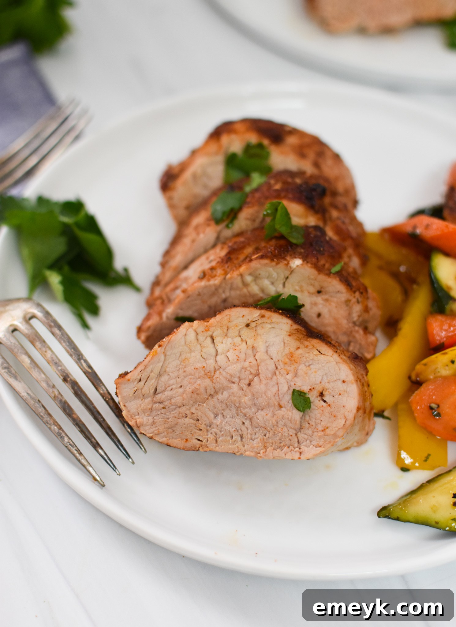 Perfectly cooked Air Fryer Pork Tenderloin, sliced and served on a white plate with a fork, ready to eat.