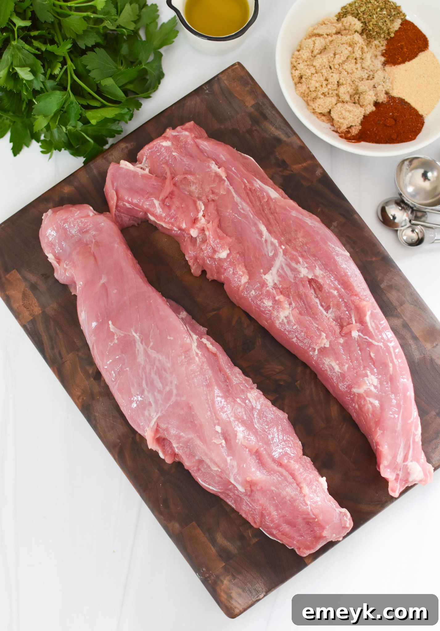 Raw pork tenderloin with a mixture of spices on a cutting board, ready for seasoning.