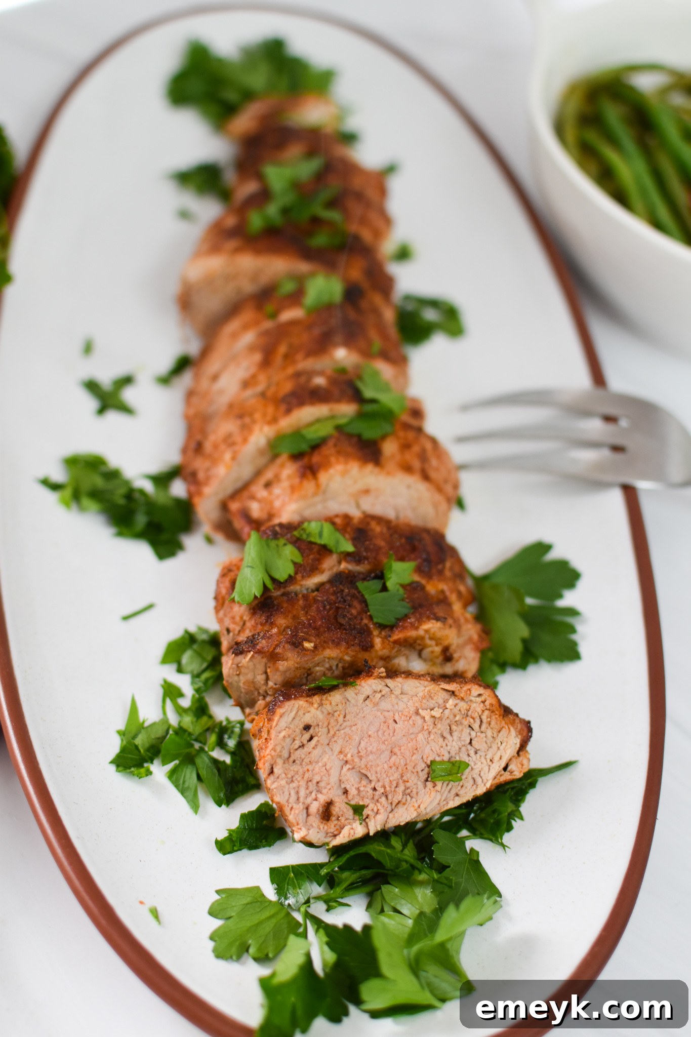 Cooked Air Fryer Pork Tenderloin resting on a white platter before slicing.