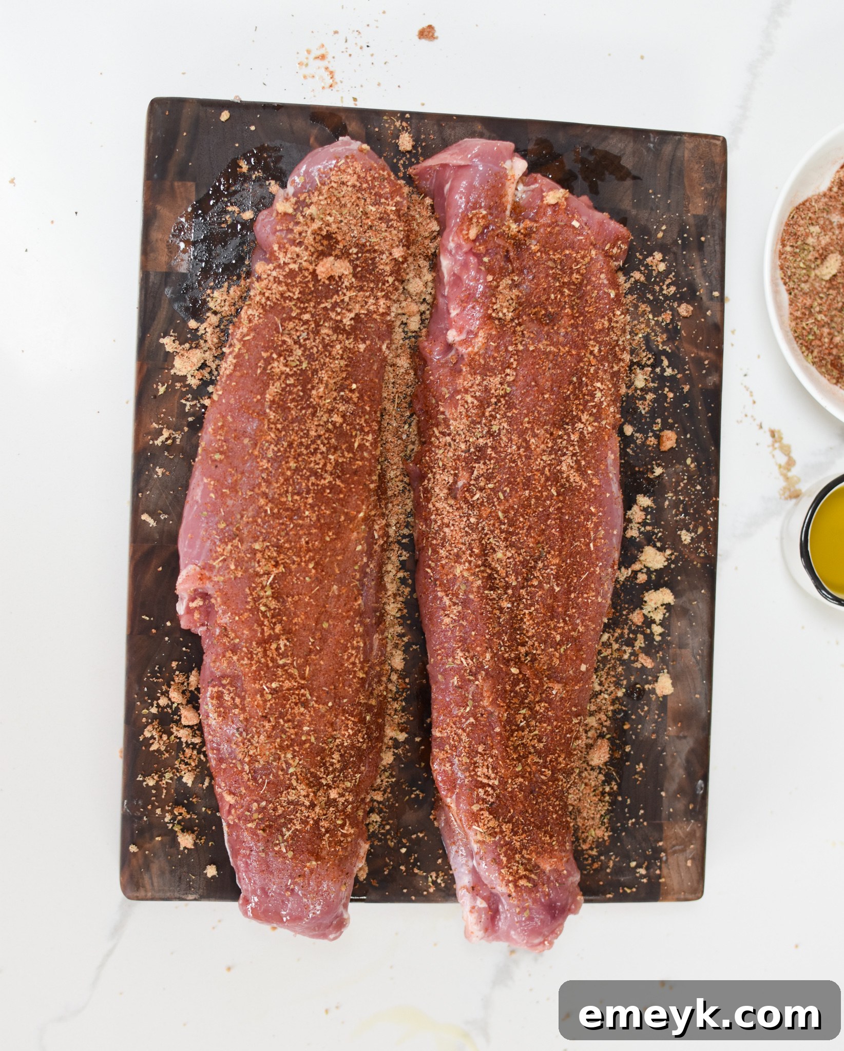 Pork tenderloin seasoned generously with a spice rub on a cutting board, prepared for air frying.