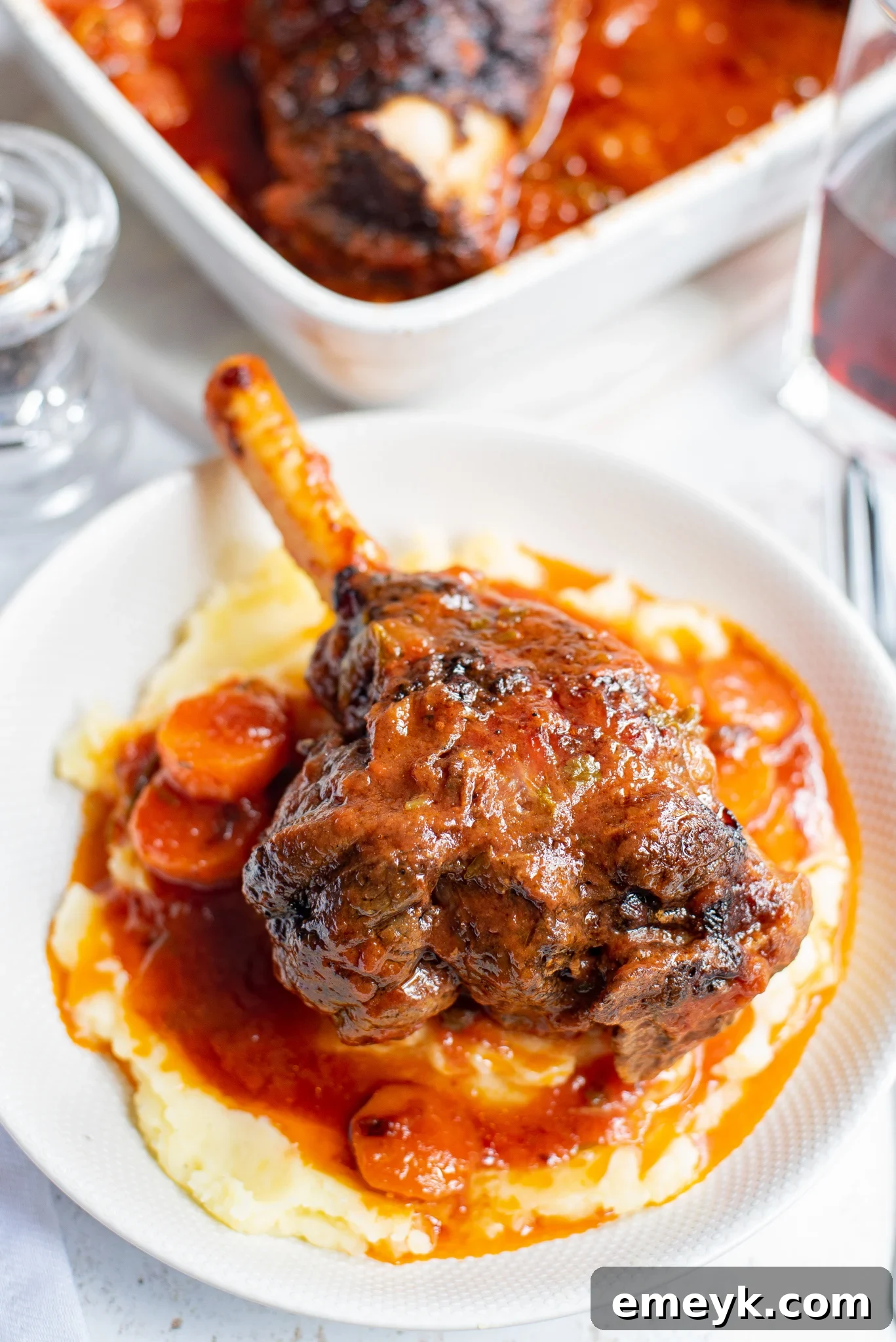 Braised Lamb Shank Recipe in a white bowl, garnished with fresh herbs.