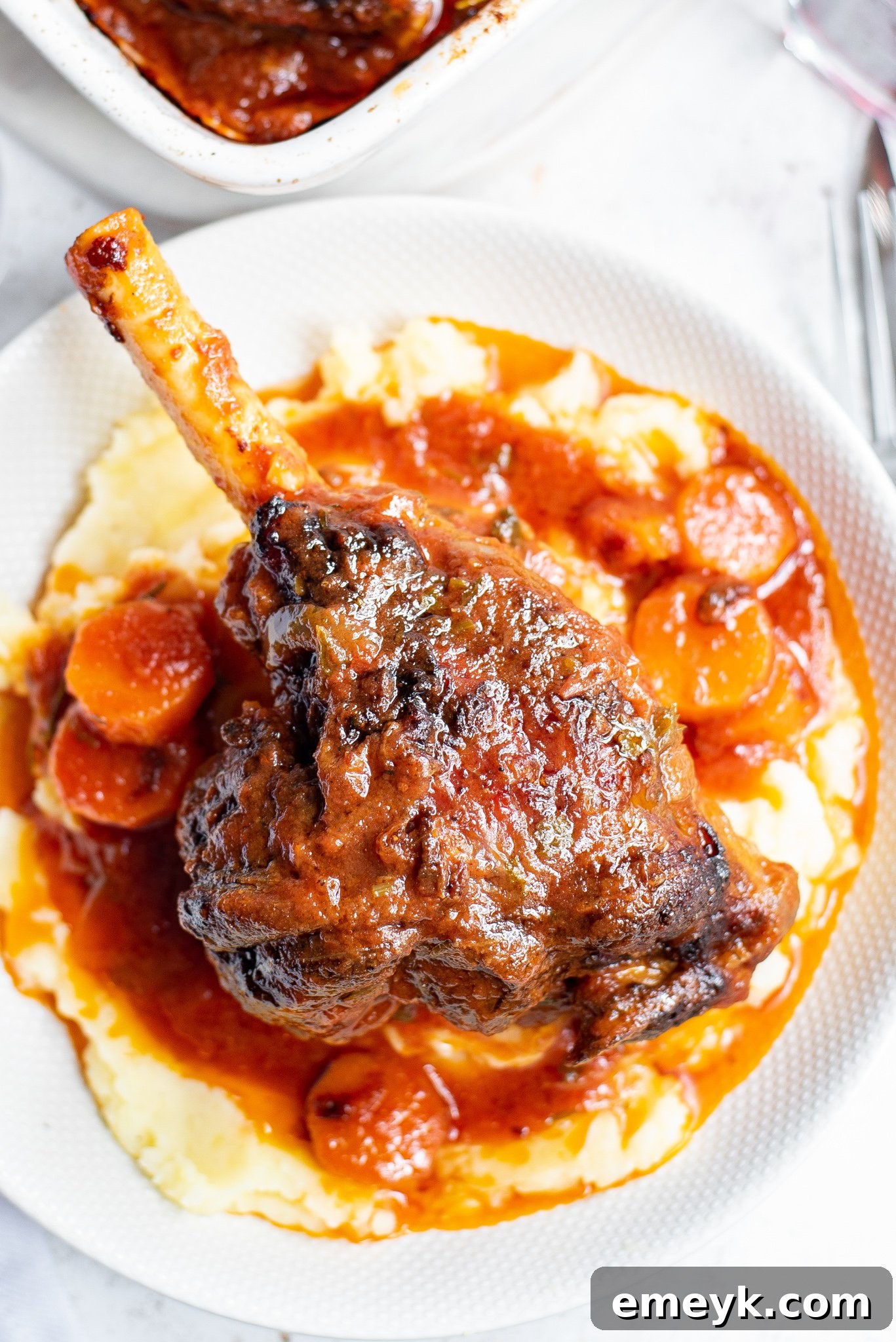 Braised Lamb Shanks Recipe with cooked carrots and rich sauce in a baking dish.