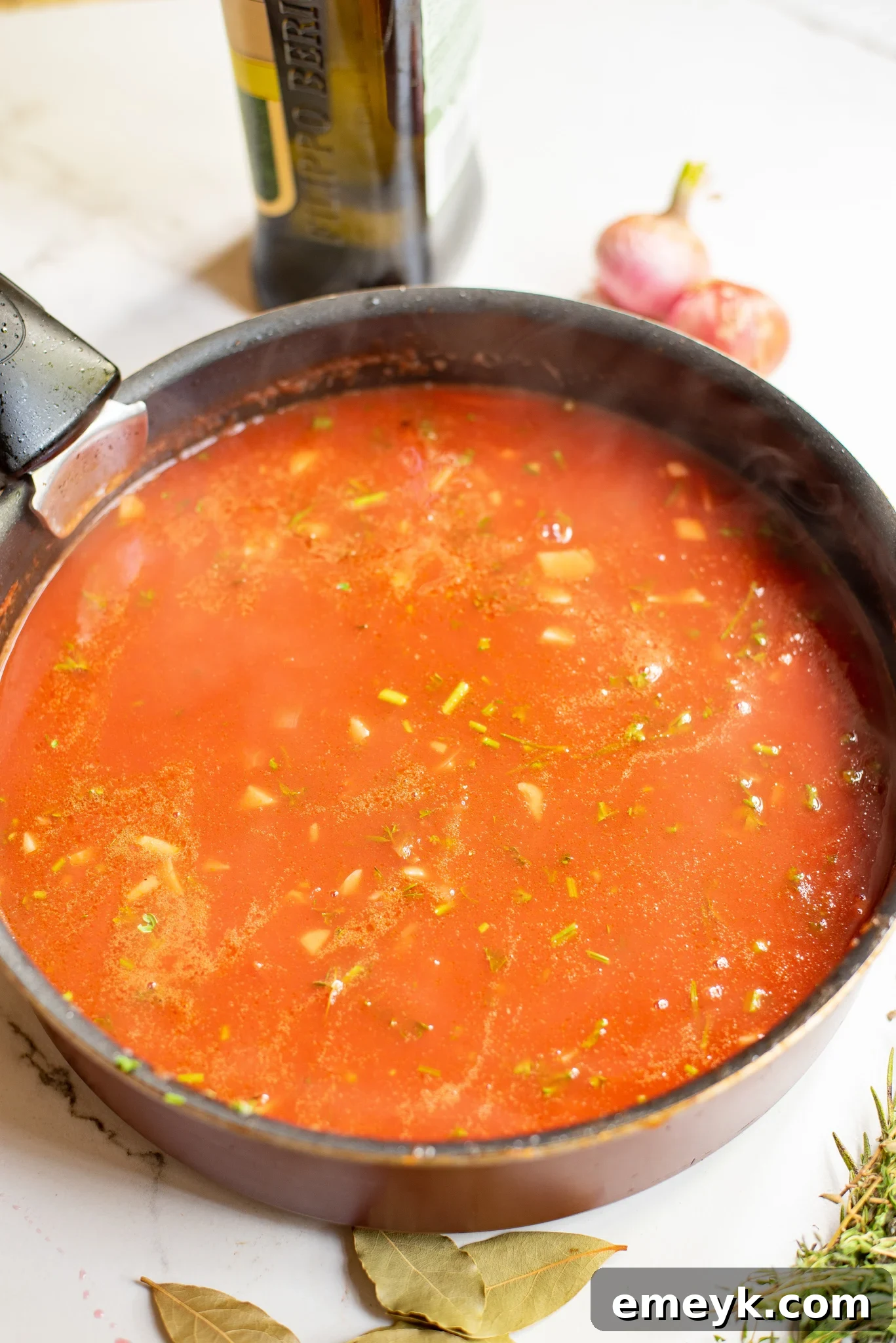 Braised Lamb Shanks Recipe with sauce and herbs in a skillet before transferring.