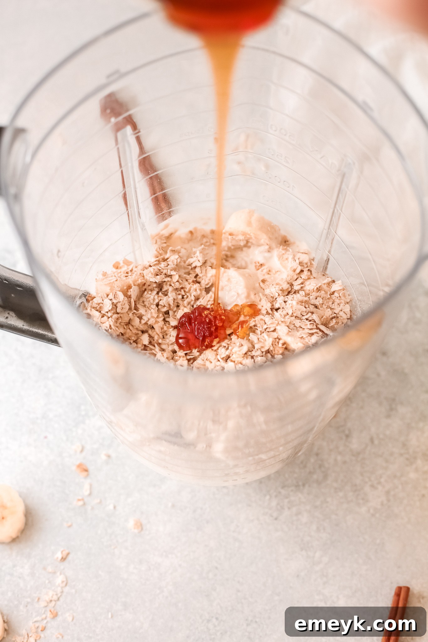 A stream of golden honey being poured into a blender with other oat smoothie ingredients.