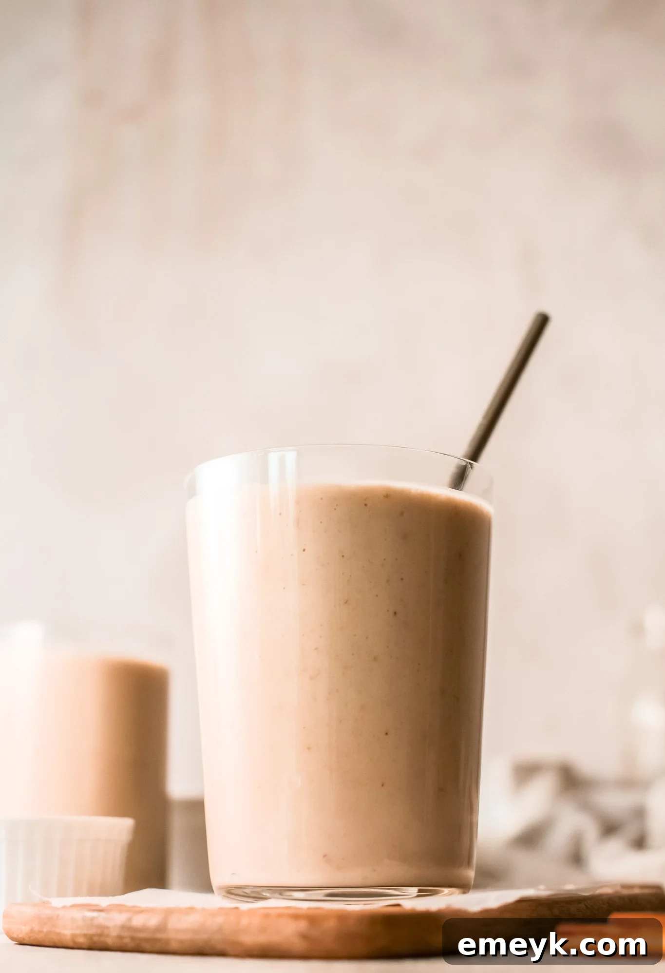 Close-up of a glass of creamy oat smoothie with a straw, garnished with a sprinkle of cinnamon.