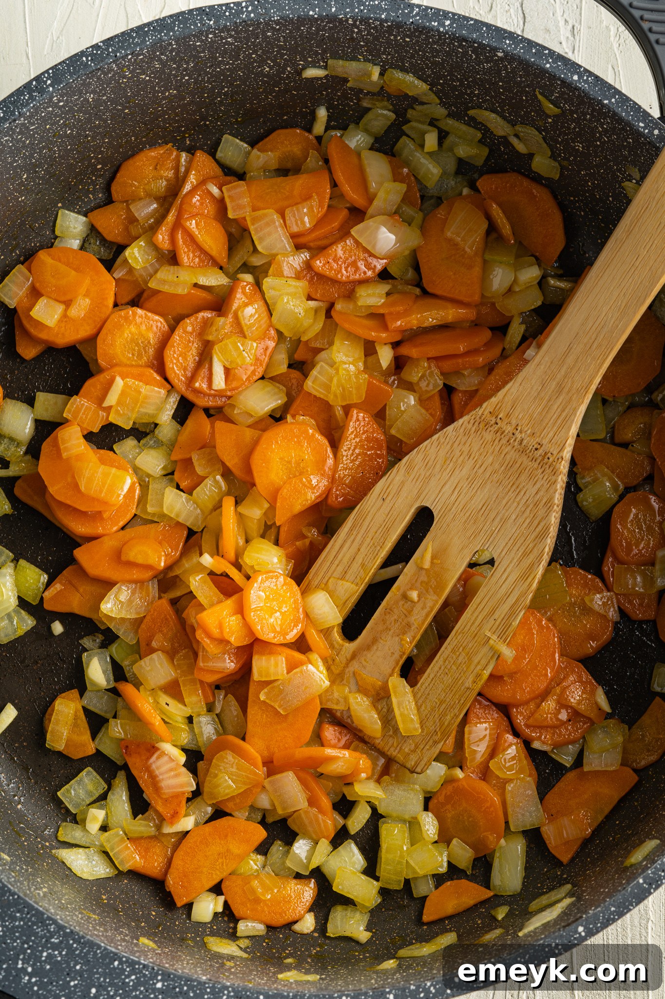 Sautéing onions, garlic, carrots, and celery in a pot with a spatula for Sweet Potato Lentil Soup.