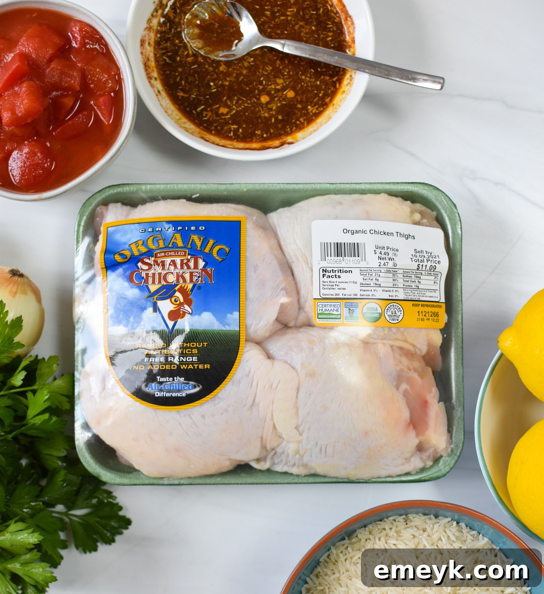 Fresh ingredients laid out for One Pot Mediterranean Chicken and Rice, including chicken thighs, rice, lemons, spinach, tomatoes, and spices.