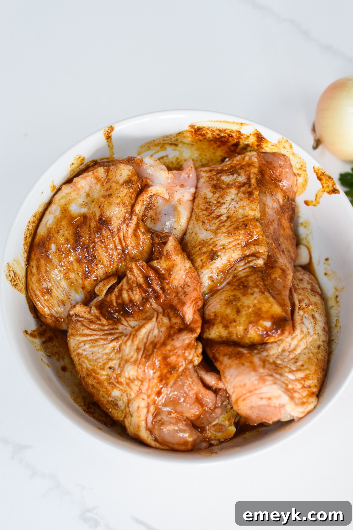 Marinated chicken thighs in a bowl, coated with Mediterranean spices, ready for cooking.