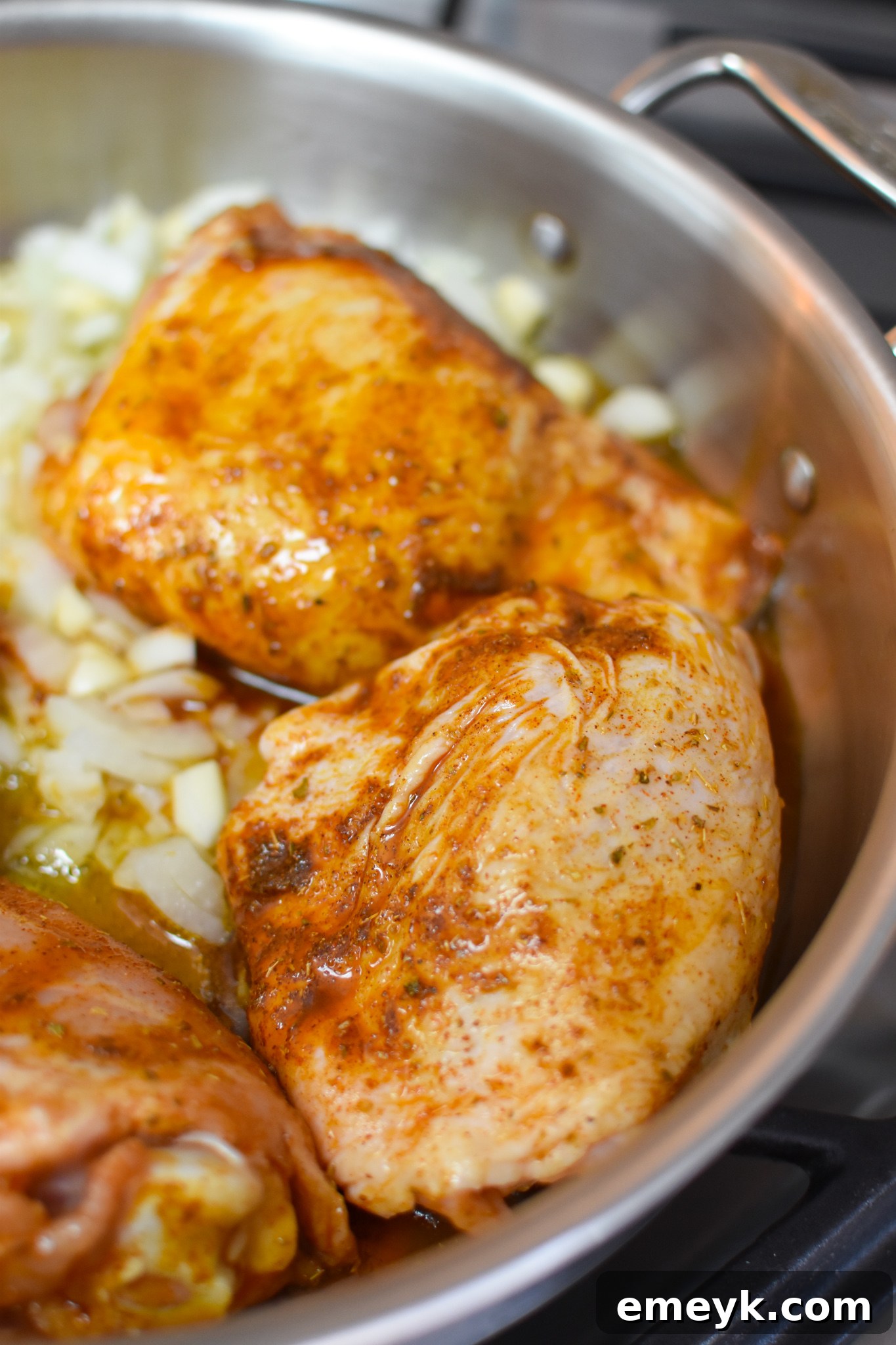 Chicken thighs searing in a skillet with garlic and onion, building a rich base for the dish.