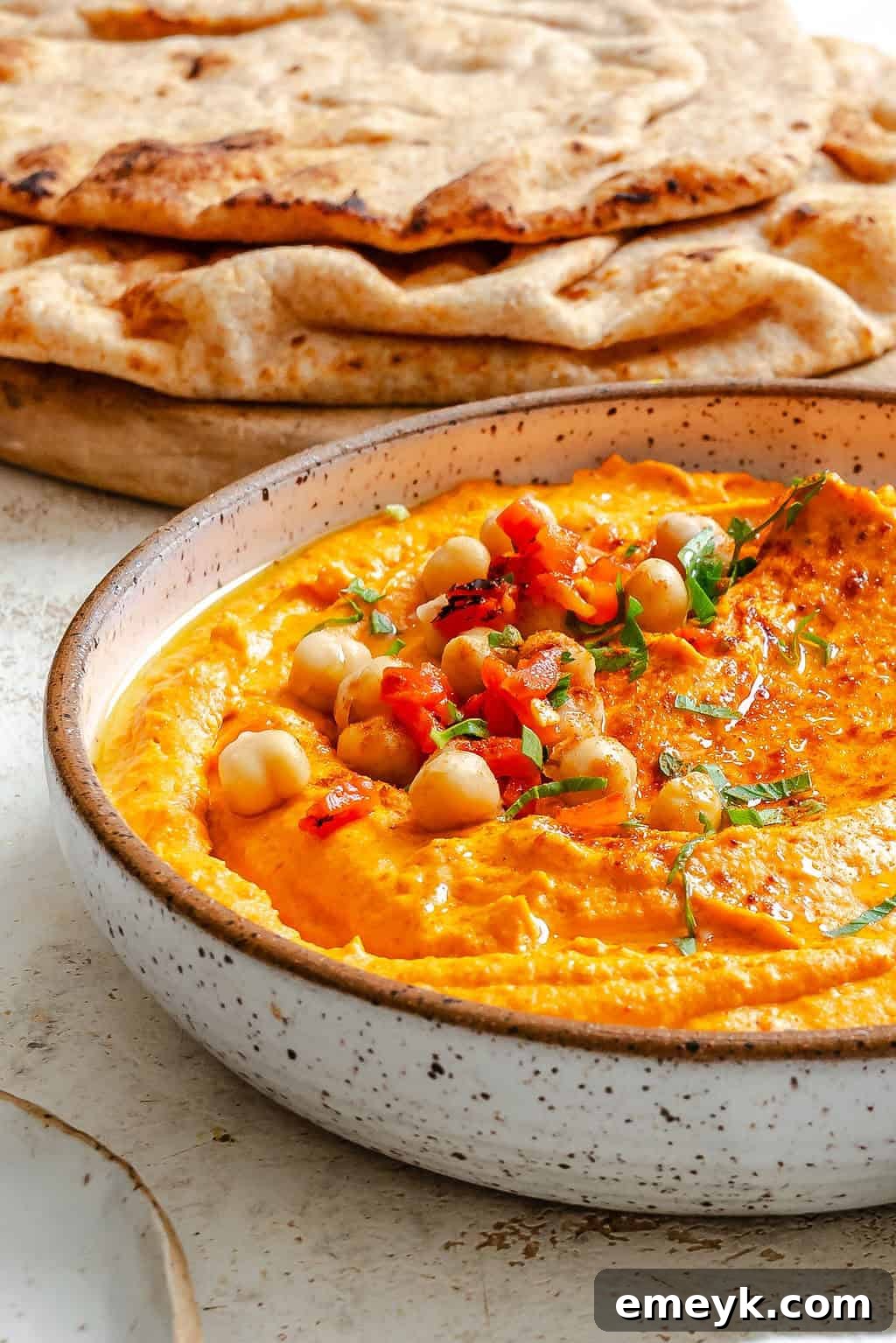 Vibrant Red Pepper Hummus 2 A beautifully presented bowl of creamy Roasted Red Pepper Hummus, garnished with fresh parsley and a delicate swirl of olive oil, accompanied by warm pita bread for dipping.
