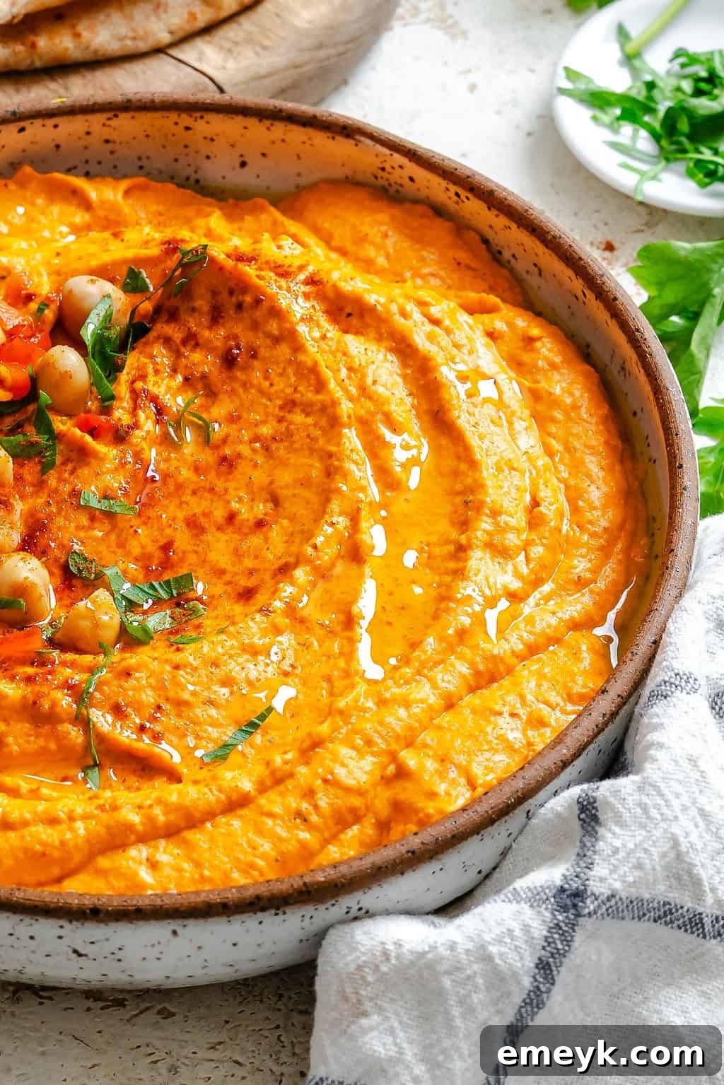 Vibrant Red Pepper Hummus 4 A close-up of freshly prepared Roasted Red Pepper Hummus in a bowl, generously garnished with whole chickpeas and freshly chopped parsley, glistening with olive oil.