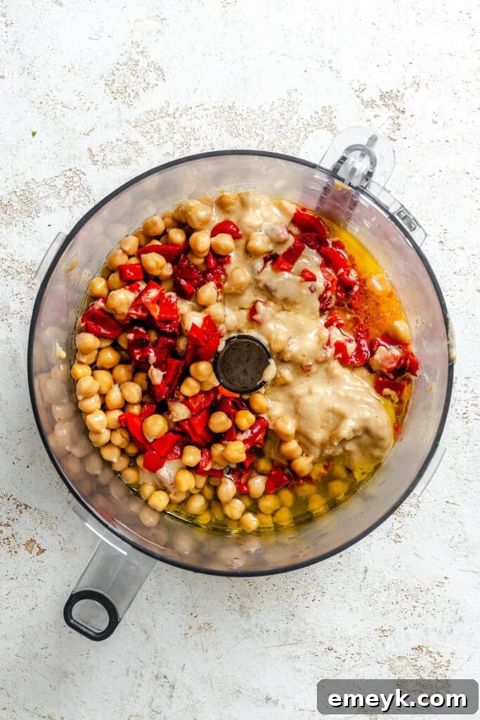 Vibrant Red Pepper Hummus 5 All the raw ingredients for Roasted Red Pepper Hummus, including chickpeas, peppers, lemon, tahini, and garlic, loaded into a food processor ready for blending.