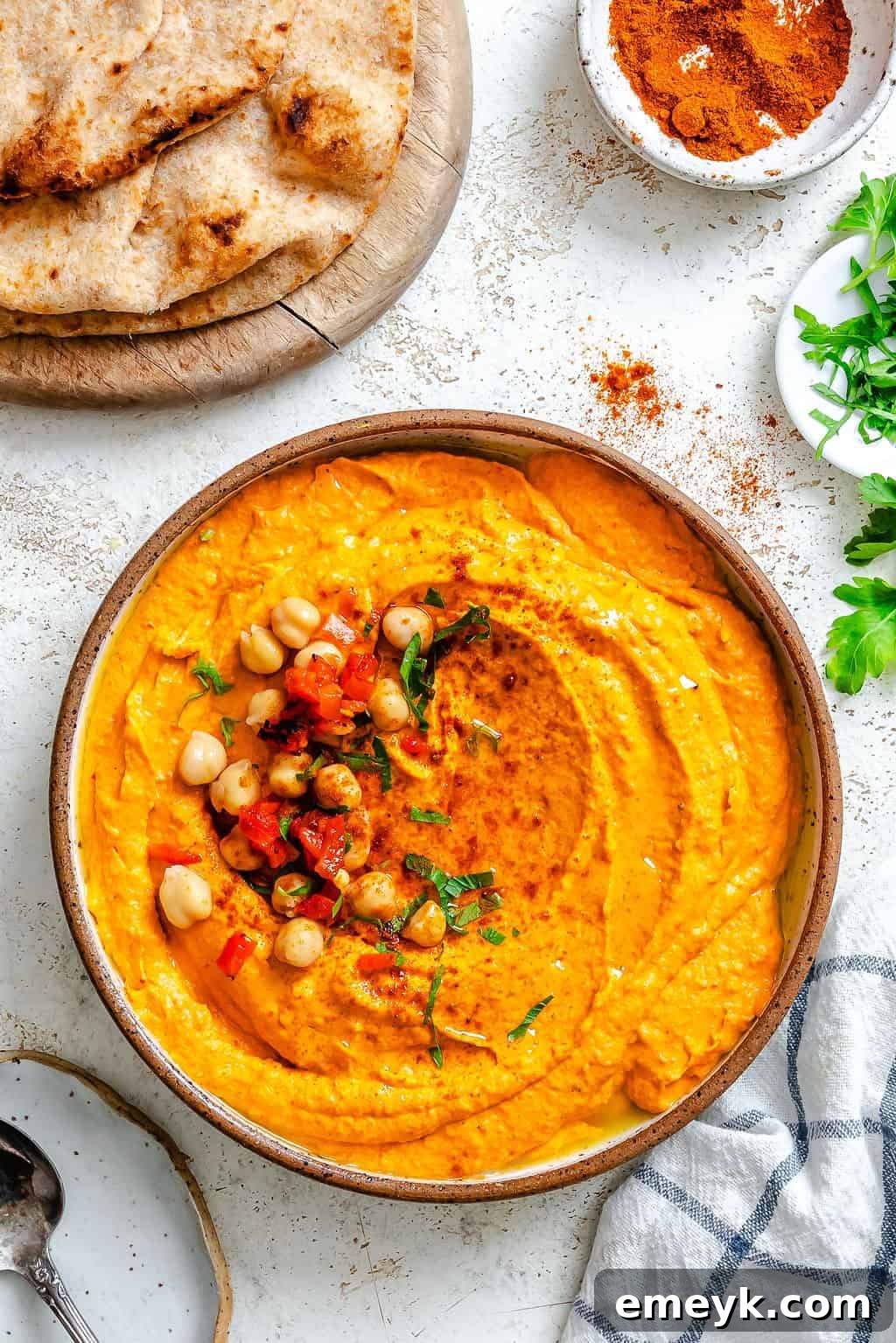 Vibrant Red Pepper Hummus 7 A close-up view of a bowl of Roasted Red Pepper Hummus, garnished with whole chickpeas and a beautiful drizzle of olive oil, showcasing its inviting texture.