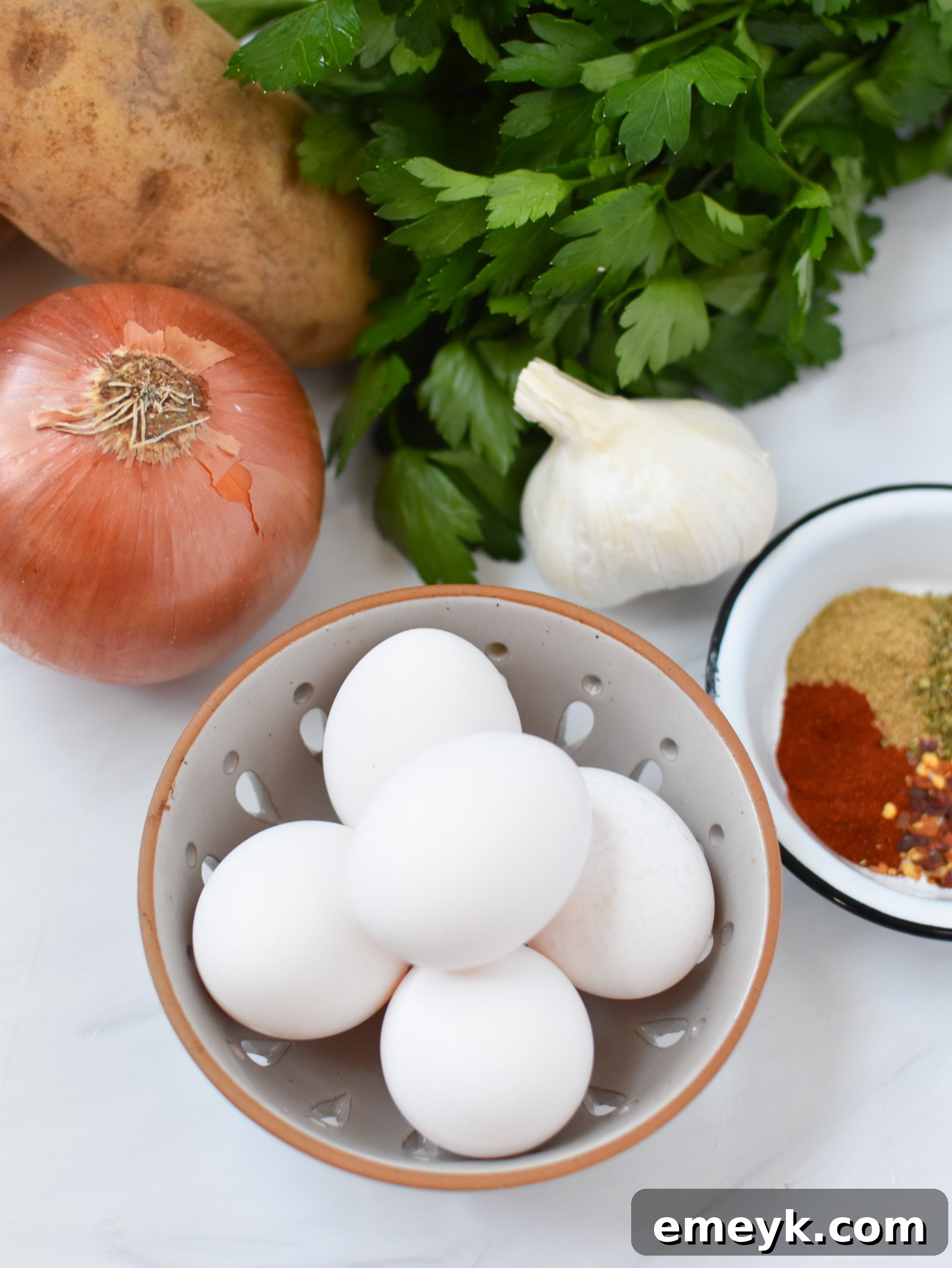 Ingredients laid out for Lebanese Potato and Egg Recipe: eggs, potatoes, onion, garlic, and spices.