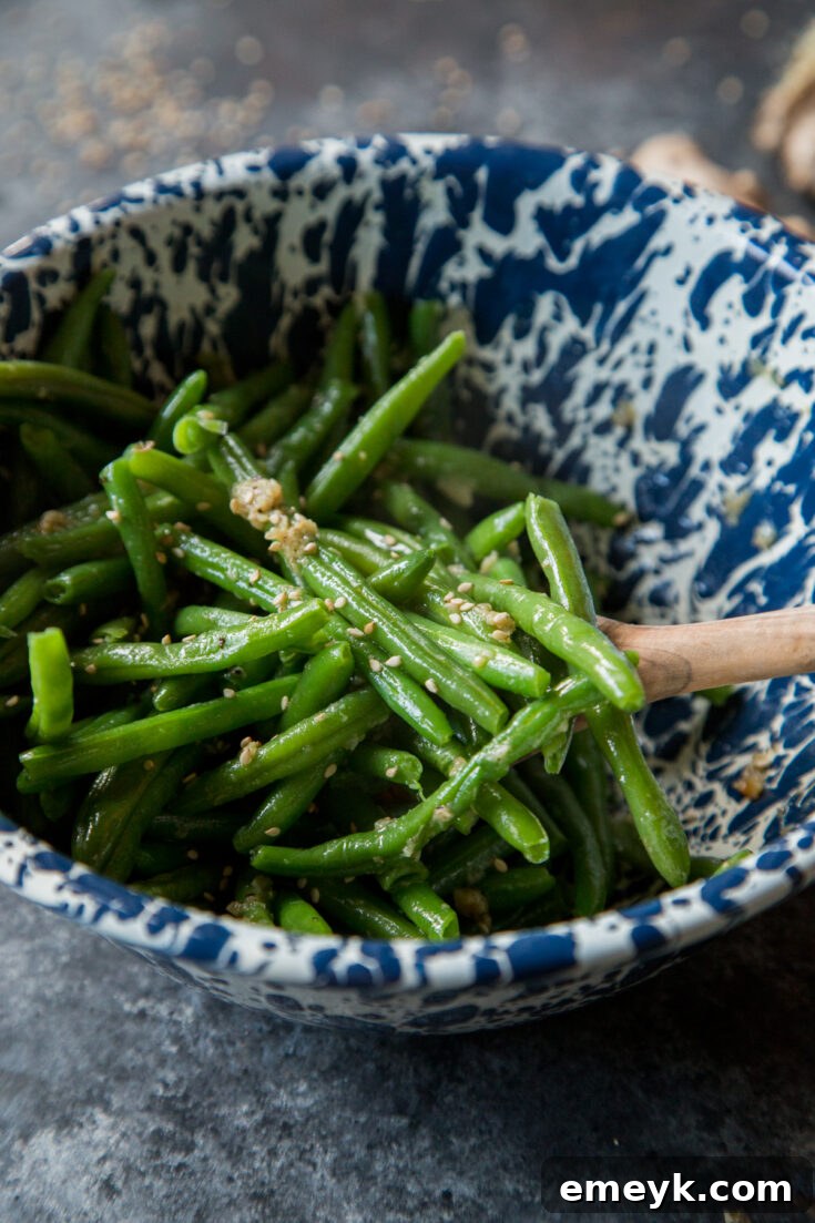 Freshly sautéed Sesame Ginger Garlic Green Beans, vibrant green and coated in an aromatic, savory sauce, presented in a rustic skillet.