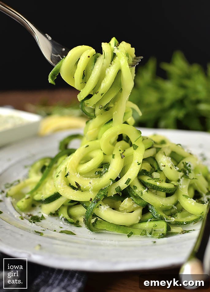 Light and healthy Parmesan Garlic-Herb Zoodles (zucchini noodles), glistening with olive oil and topped with grated Parmesan cheese and fresh herbs.