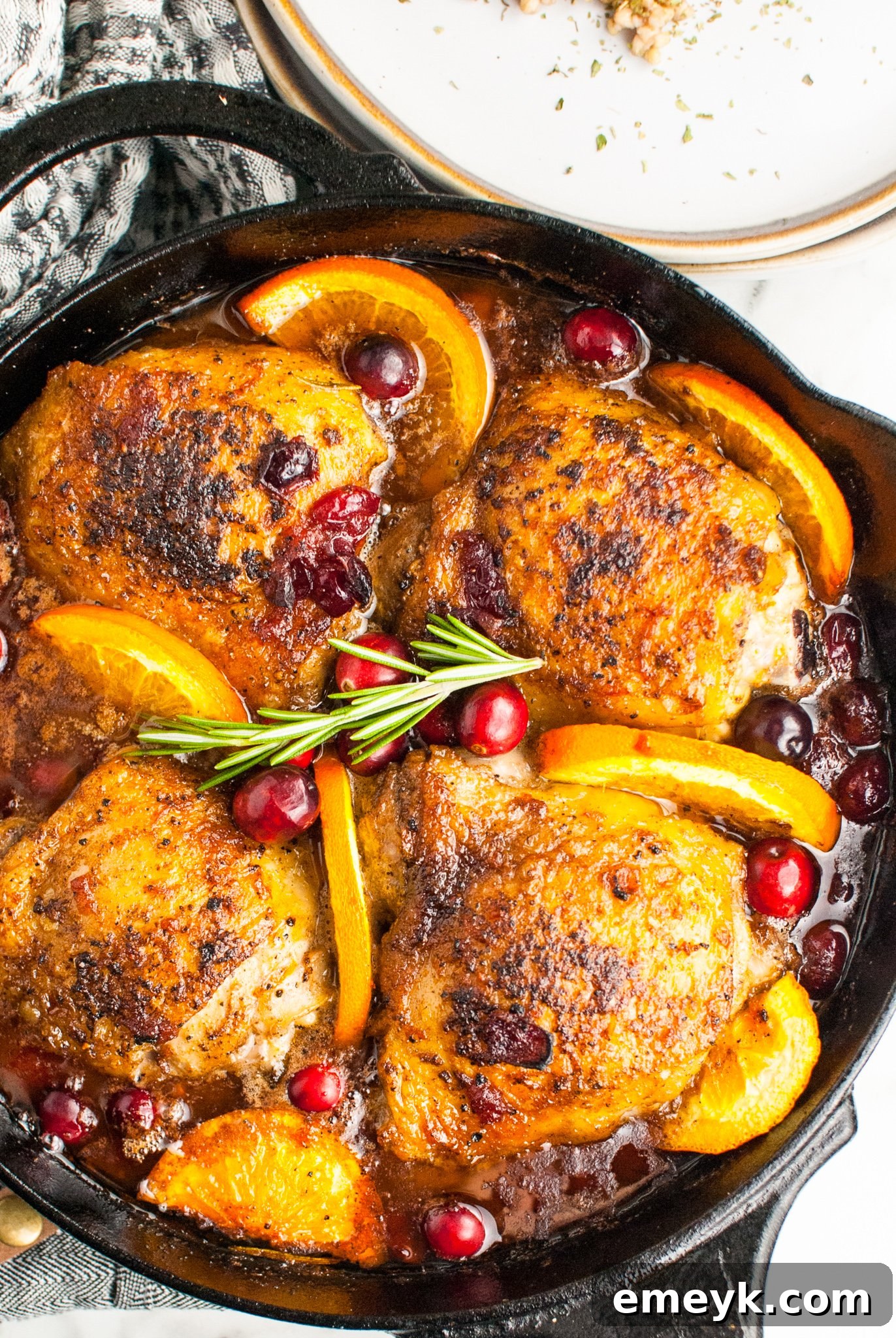 Easy Baked Chicken Thighs in a cast iron skillet, garnished with fresh cranberries and rosemary.