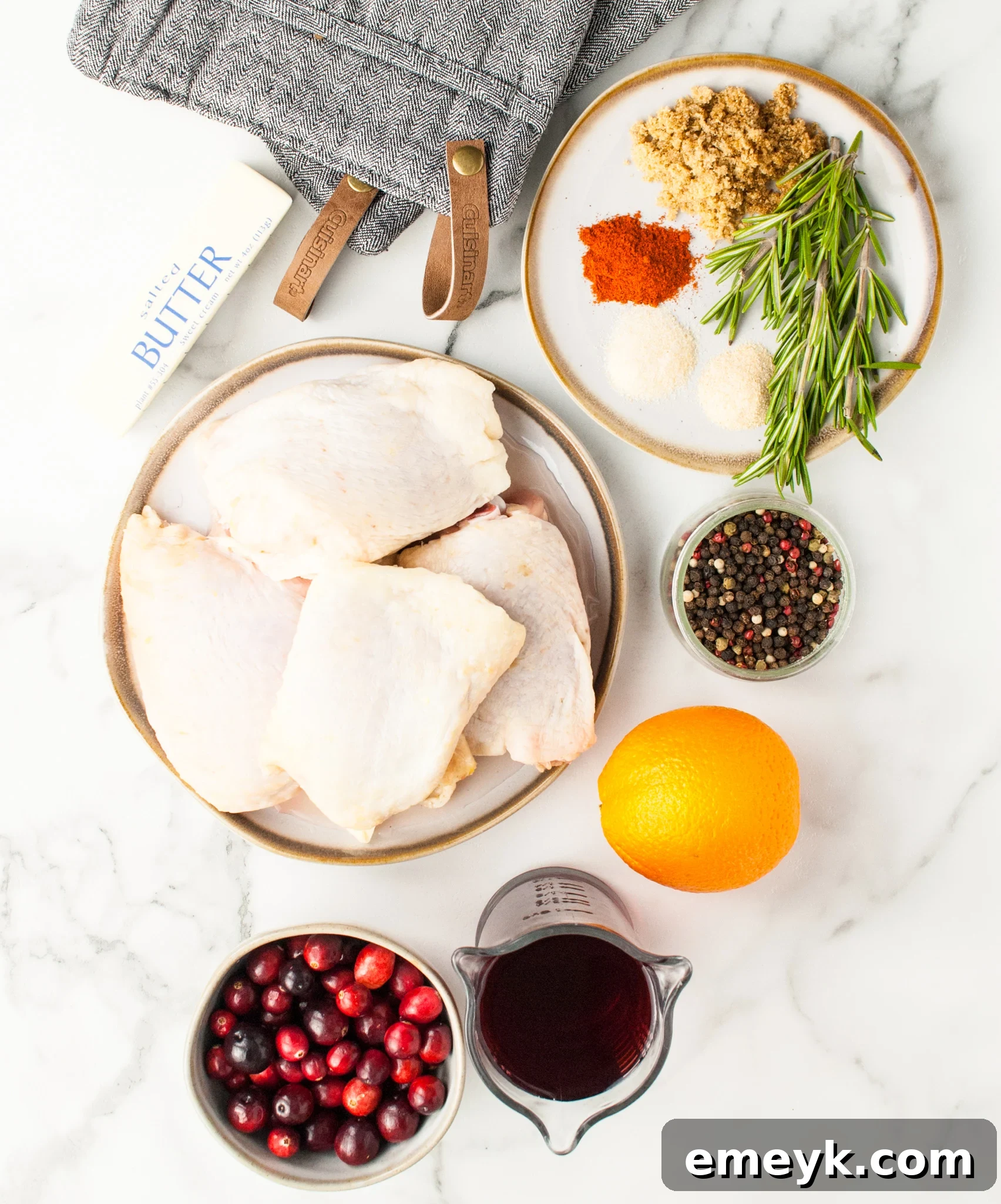 Ingredients for Easy Baked Chicken Thighs, including cranberries, oranges, chicken thighs, and spices arranged for cooking.
