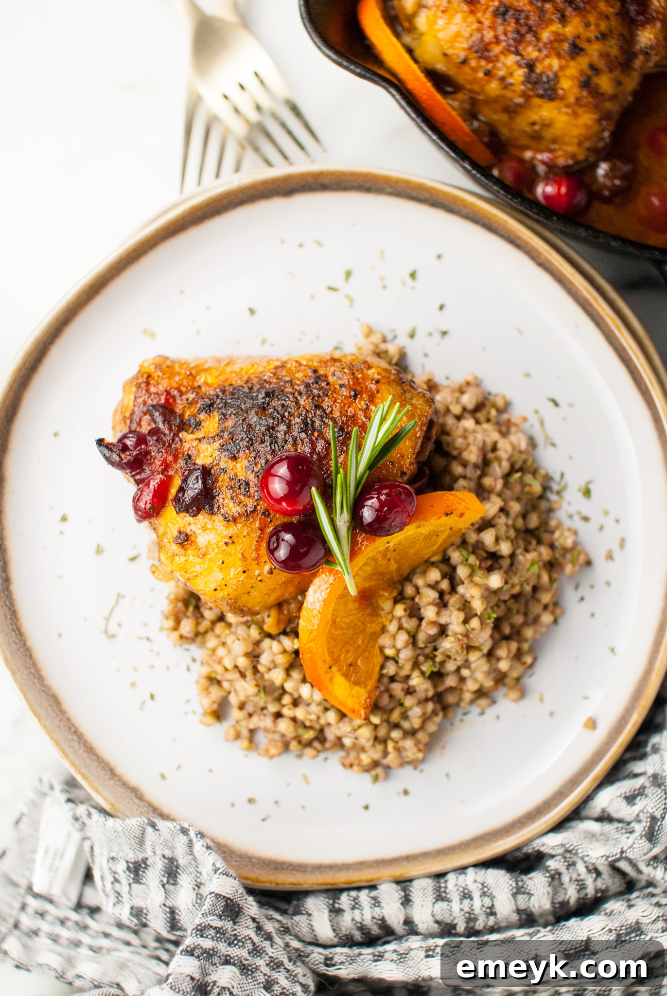 Easy Baked Chicken Thighs served on a white plate with fresh herbs and orange slices.
