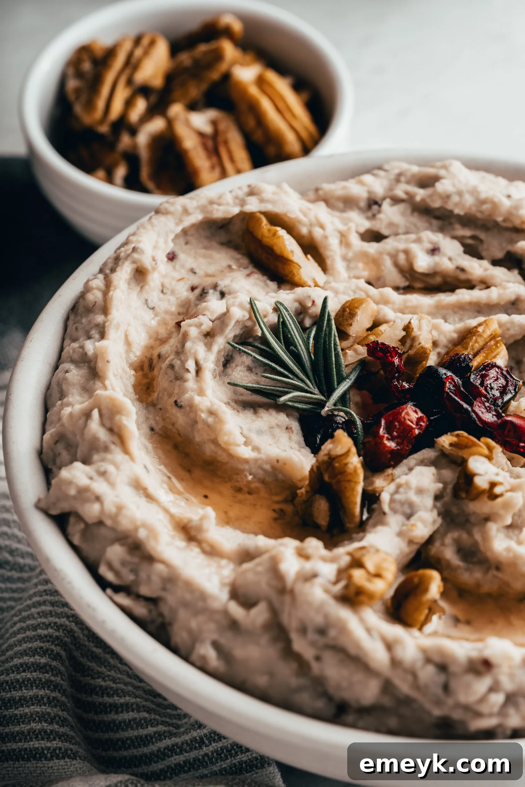 Creamy White Bean Hummus with Cranberry, garnished with fresh rosemary and chopped pecans, served in an elegant white bowl.