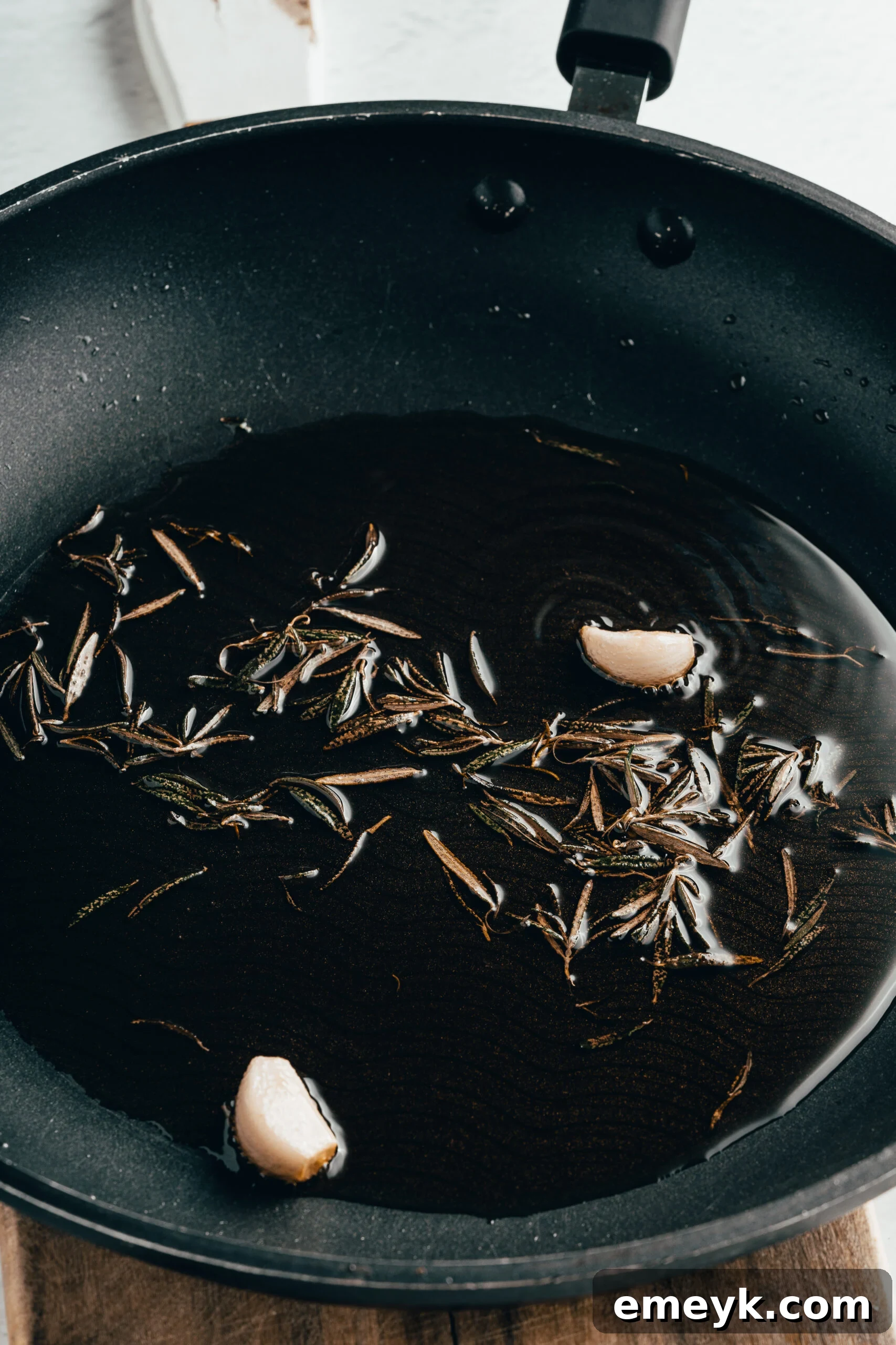 Olive oil infused with fresh rosemary and garlic cloves simmering gently in a small skillet, a key step for aromatic White Bean Hummus.