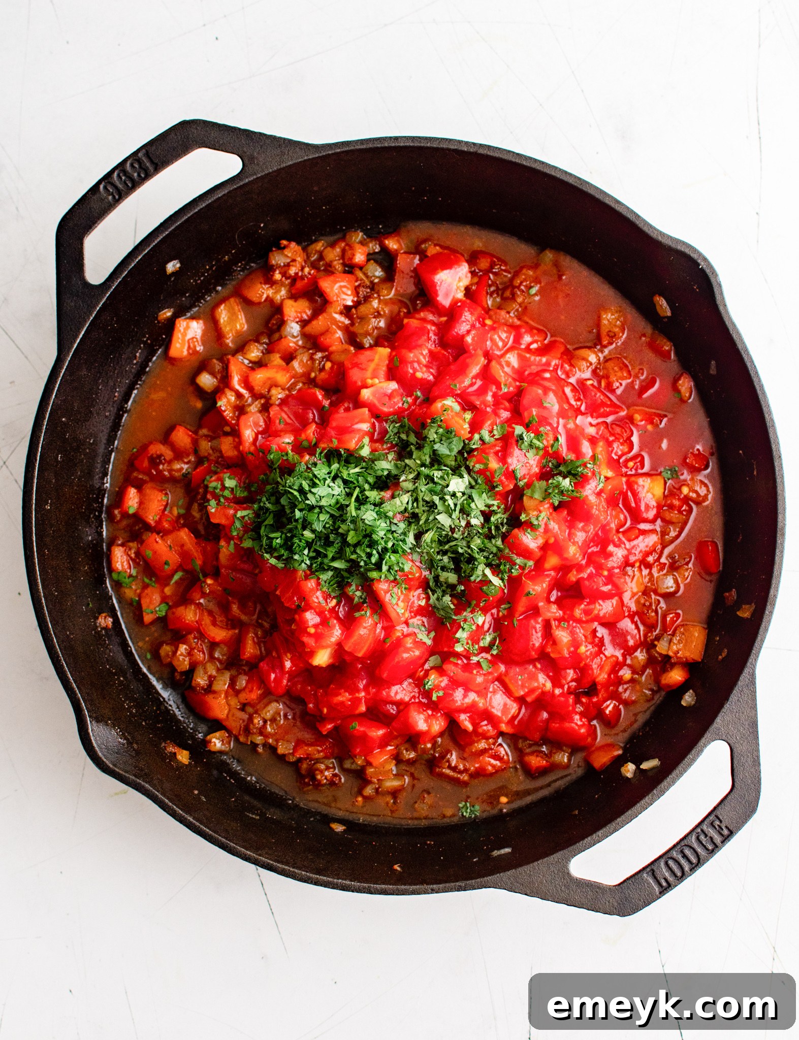 Tomatoes and fresh herbs added to the sautéed vegetables in a skillet for shakshuka.
