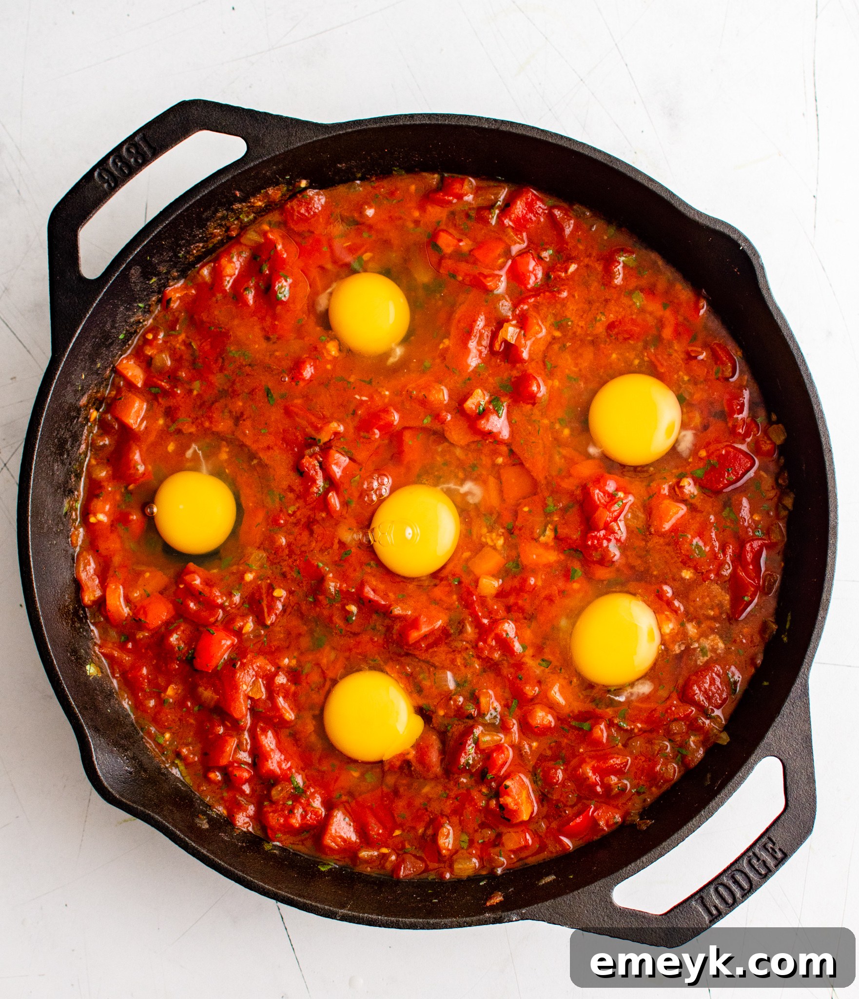 Eggs cracked into the simmering tomato sauce in a skillet for shakshuka.