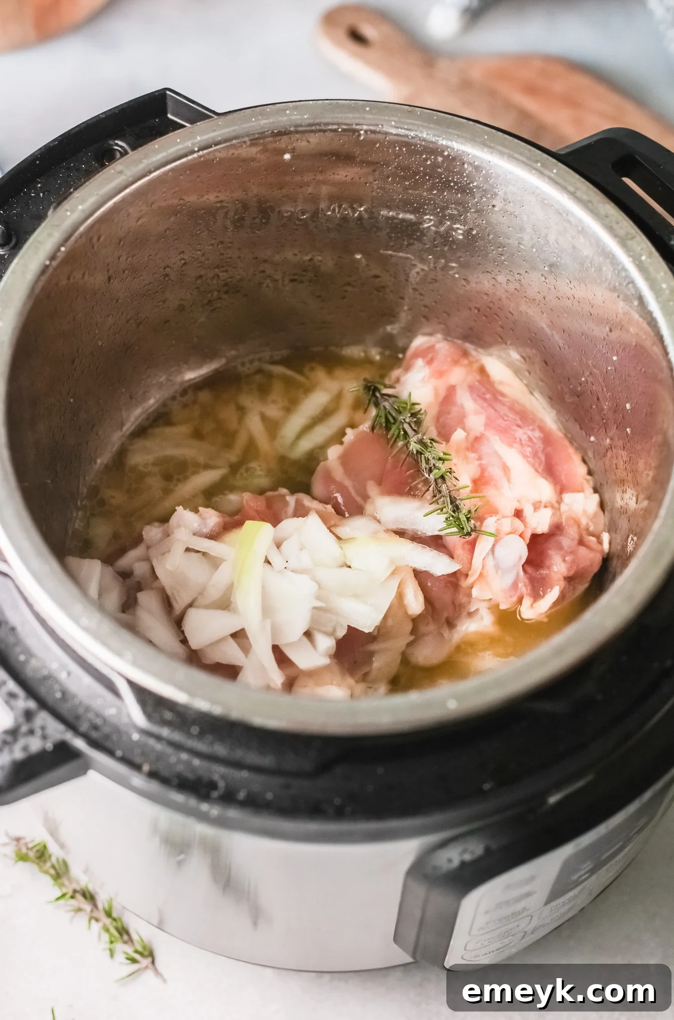 Instant Pot Creamy Rosemary Chicken with broth and rosemary sprigs added.