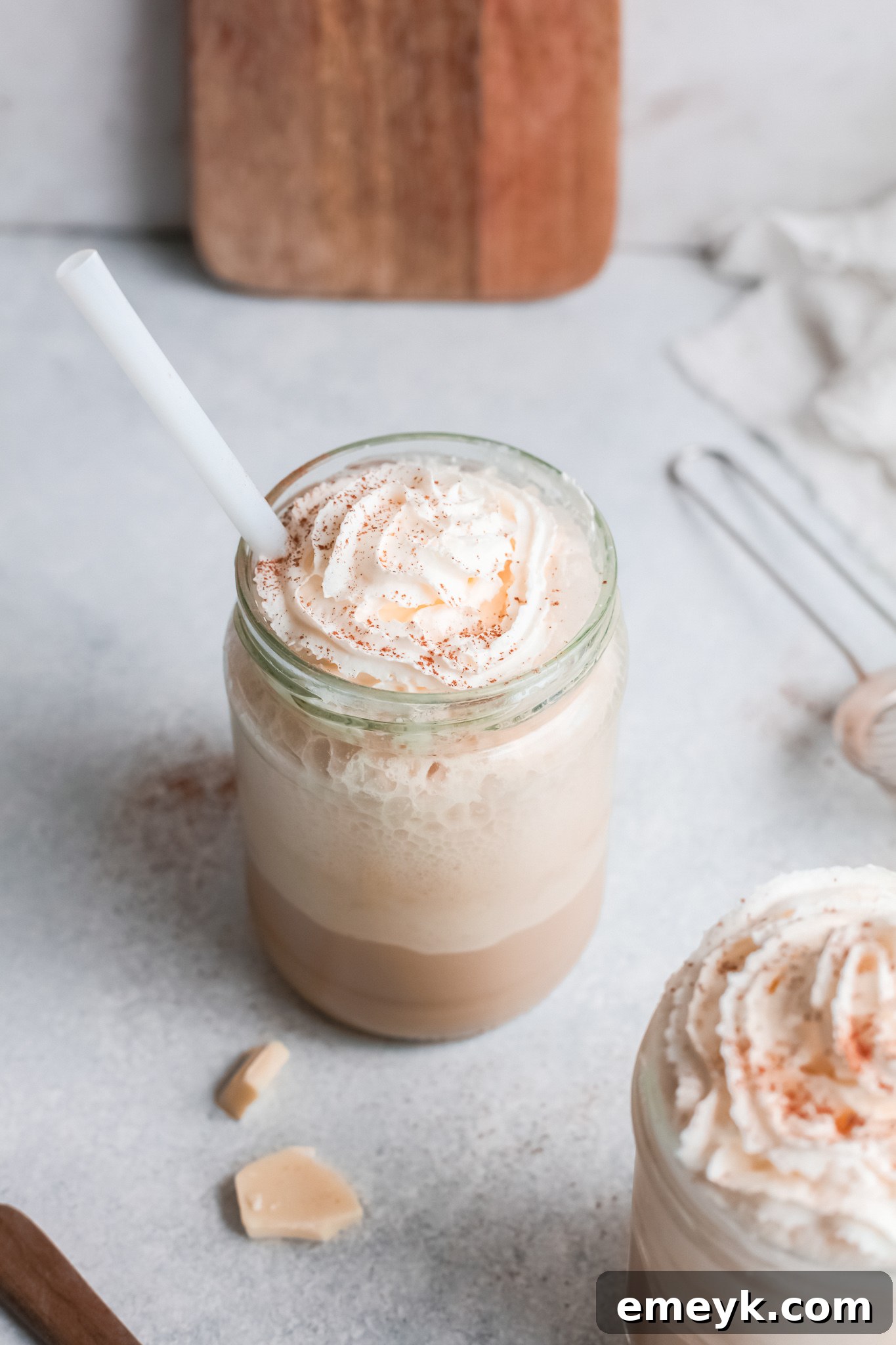 A tall glass filled with a White Chocolate Frappuccino, beautifully topped with whipped cream and a single straw, ready to be savored.