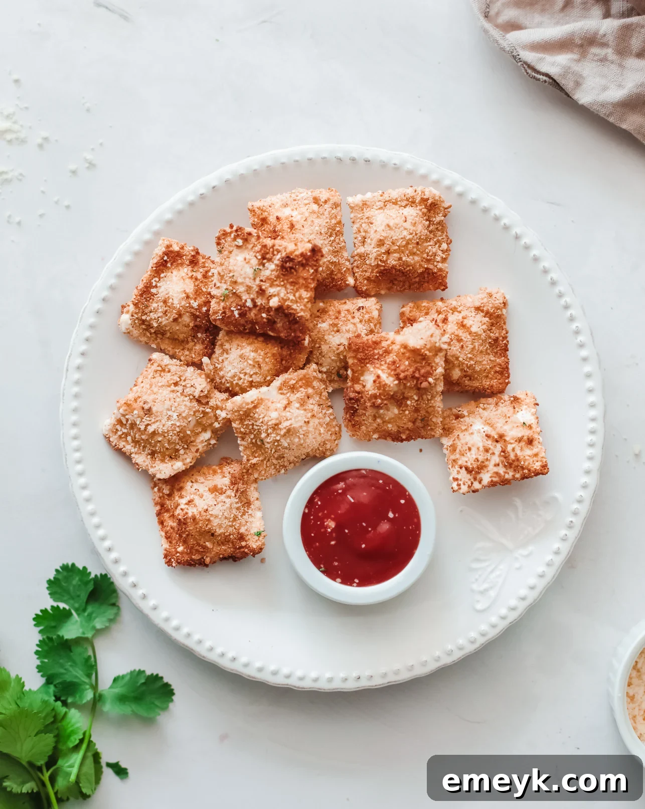 Crispy Air Fryer Ravioli 2 Golden brown air fried ravioli on a white plate, garnished with fresh herbs.