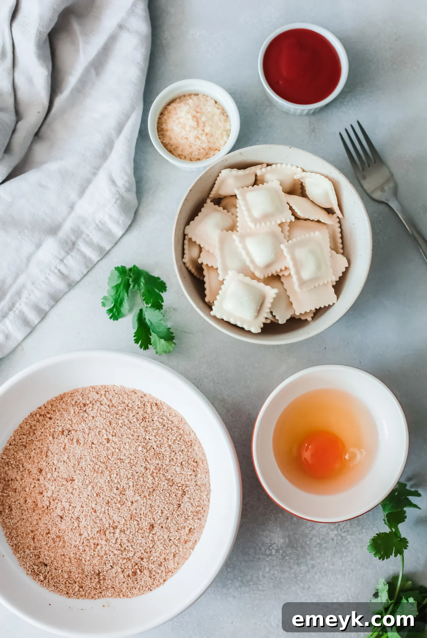 Crispy Air Fryer Ravioli 3 Ingredients for Air Fried Ravioli laid out on a table, including fresh ravioli, eggs, breadcrumbs, and spices.