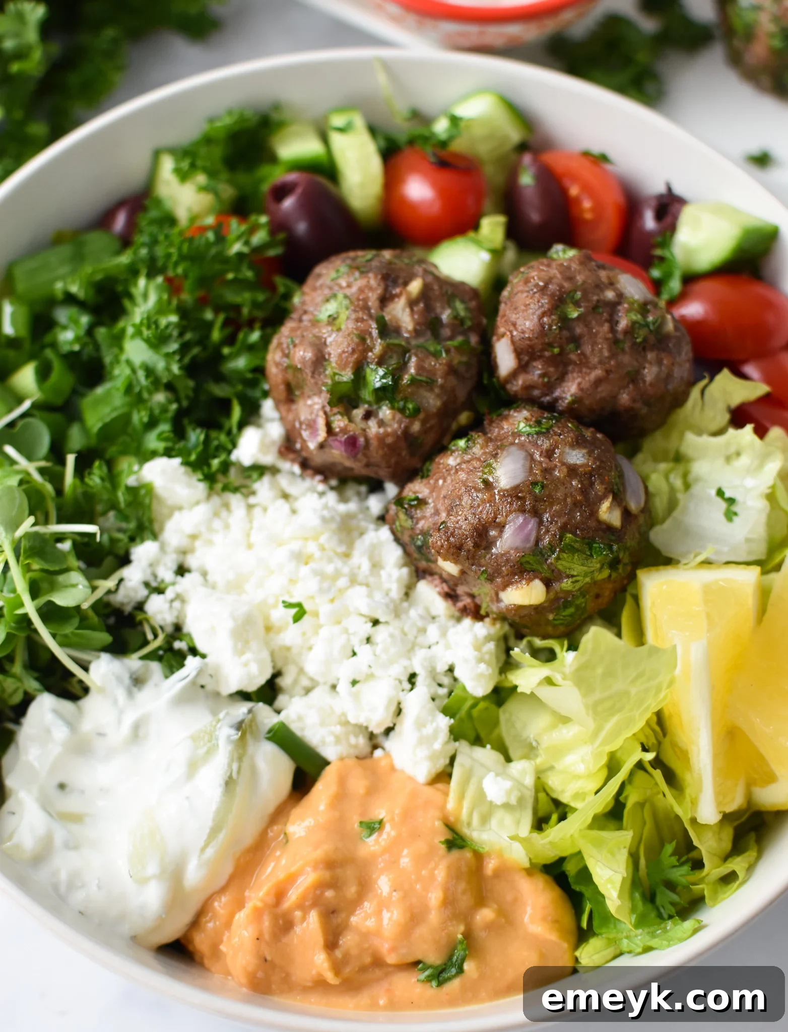 Mediterranean Baked Beef Meatballs in a hummus bowl, garnished with fresh herbs.