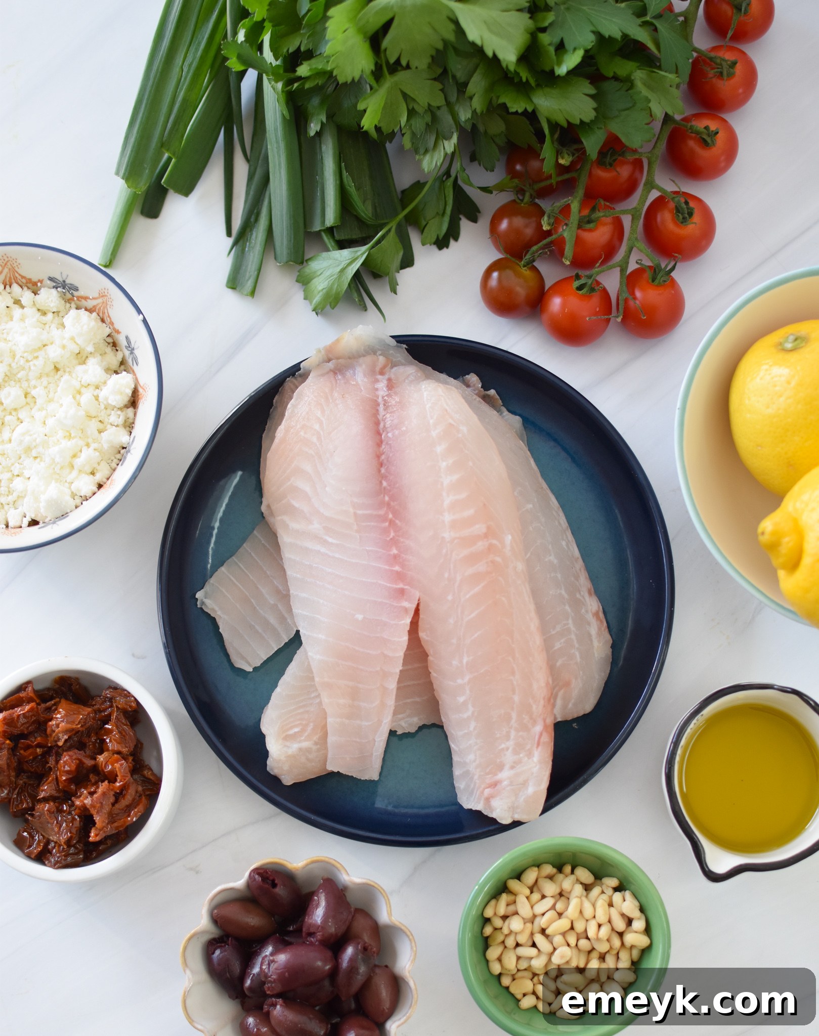 Assortment of fresh ingredients including tilapia fillets, lemon, olives, and spices for Greek Baked Tilapia.